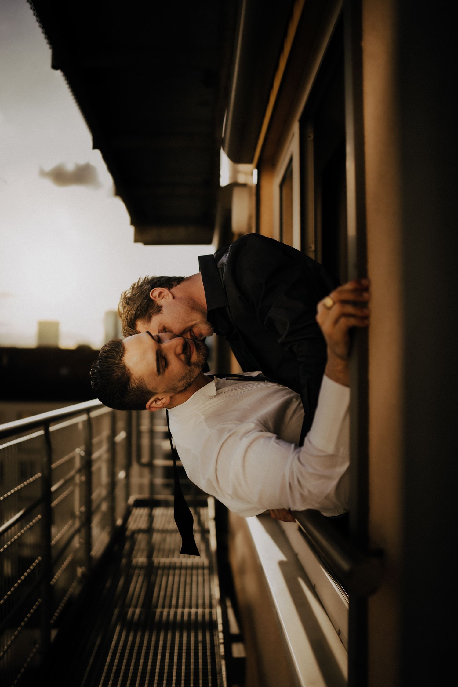 Romantic couple sharing an intimate moment on a balcony at sunset with dramatic lighting.