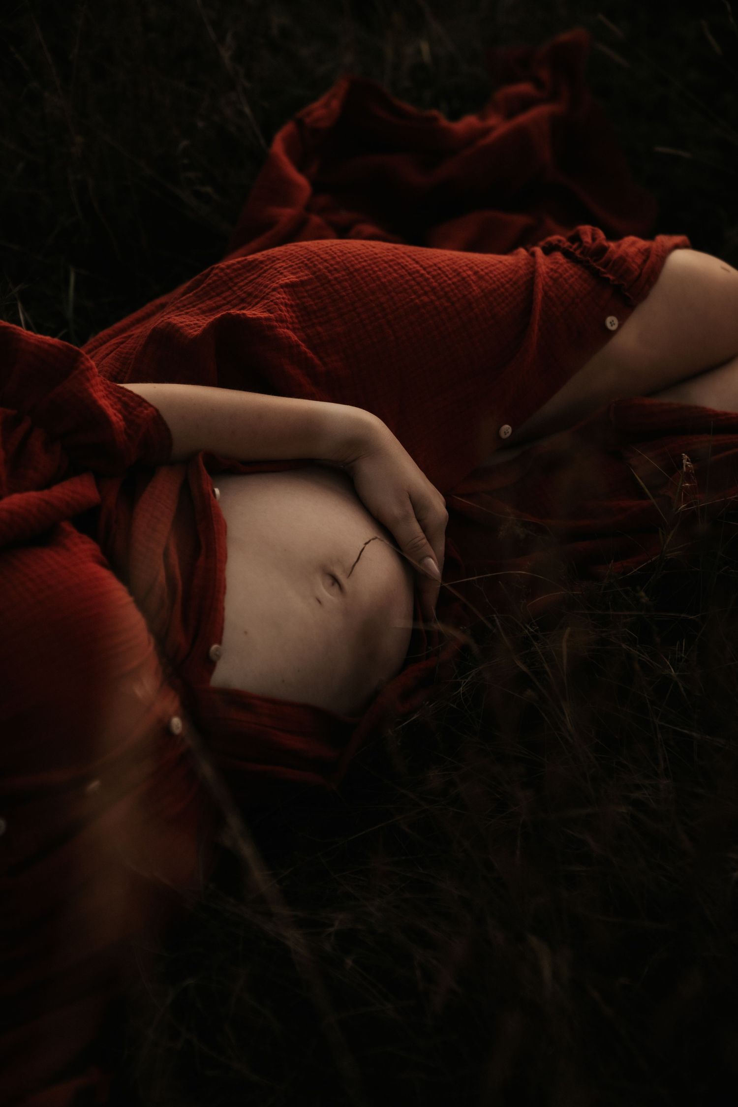 Artistic portrait of a person in a flowing red dress lying on dark ground.
