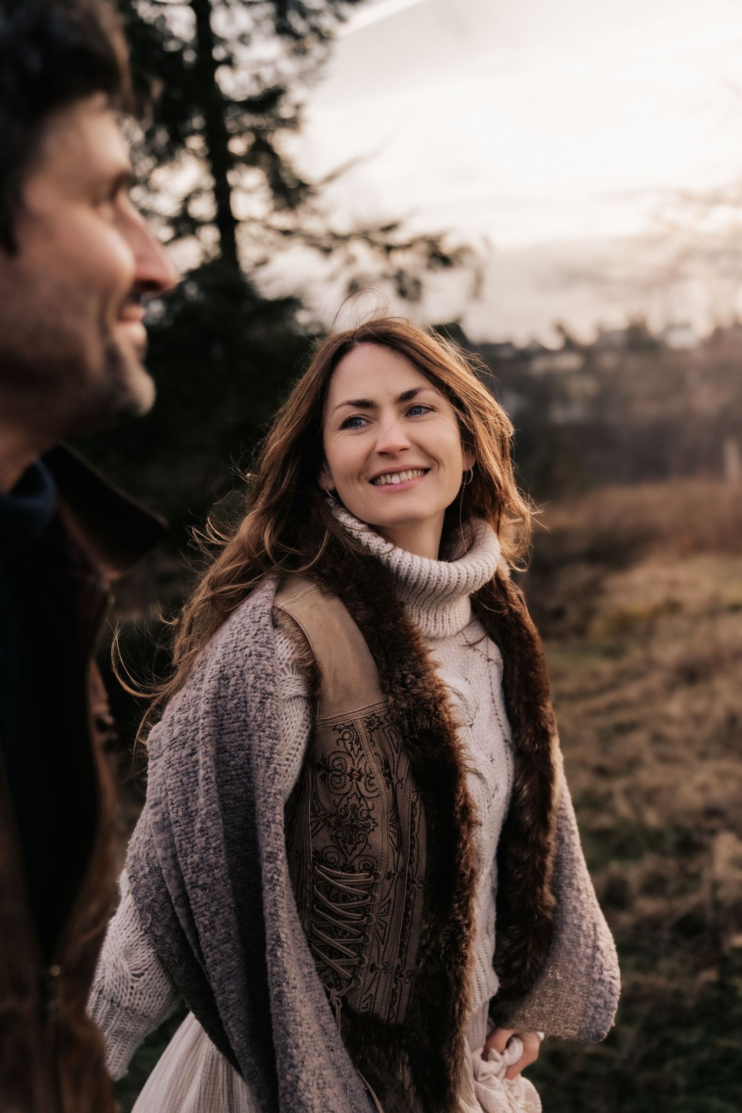 People wearing cozy sweaters share a warm moment outdoors during golden hour in a natural autumn setting.
