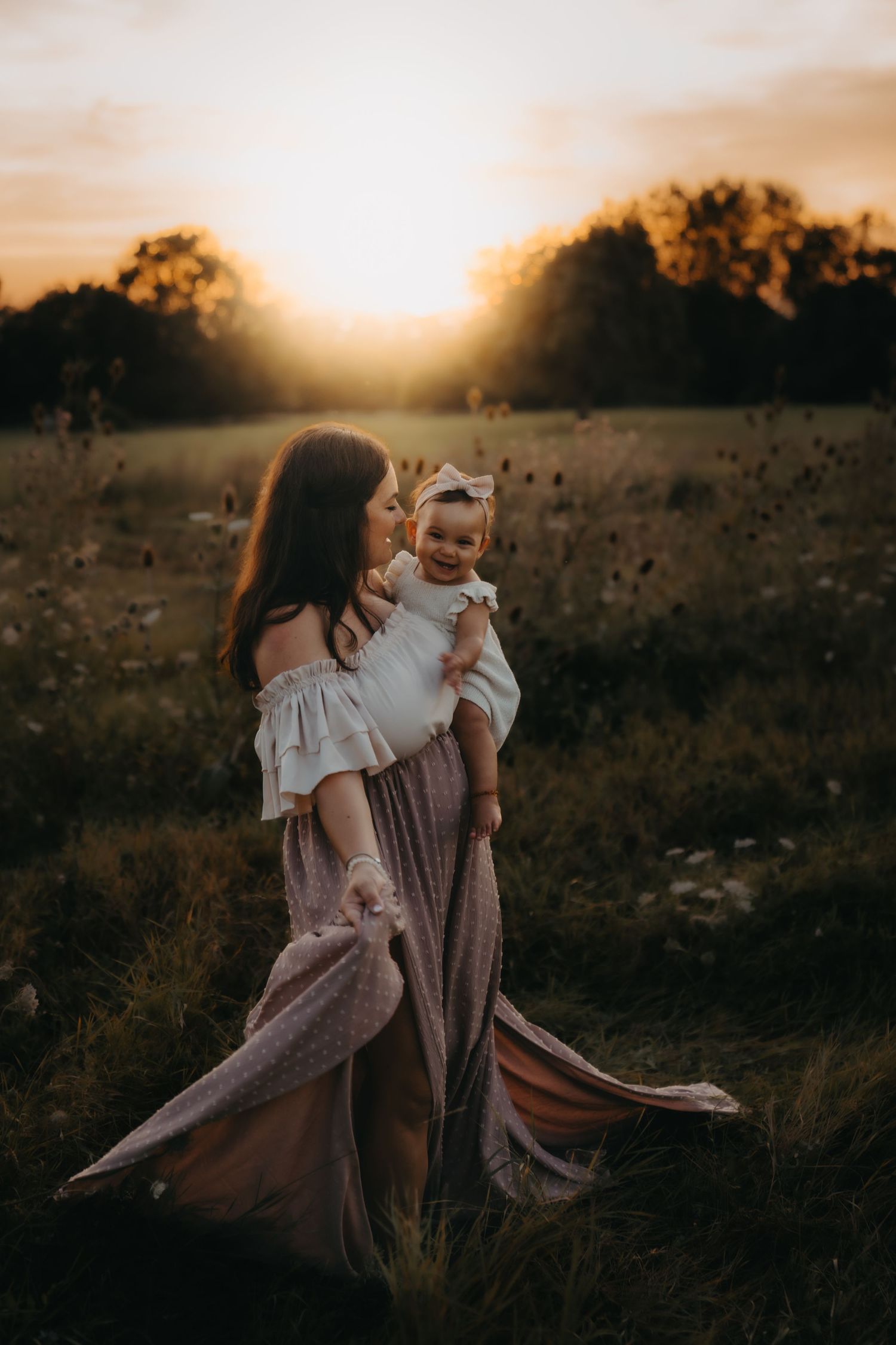 A tender sunset moment captured in a field with flowing dresses and warm golden light.