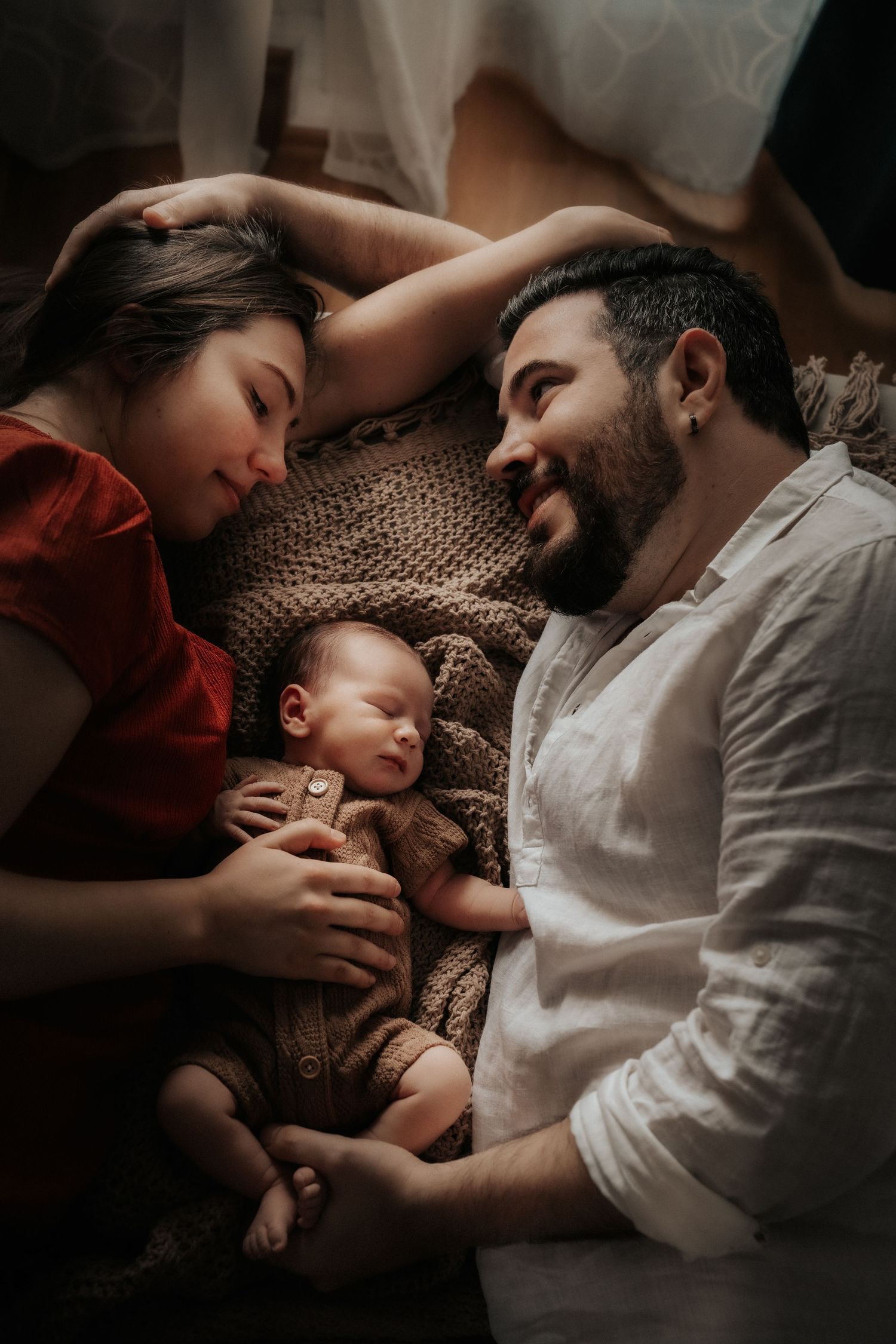 Intimate family moment as parents and baby rest together on textured bedding.