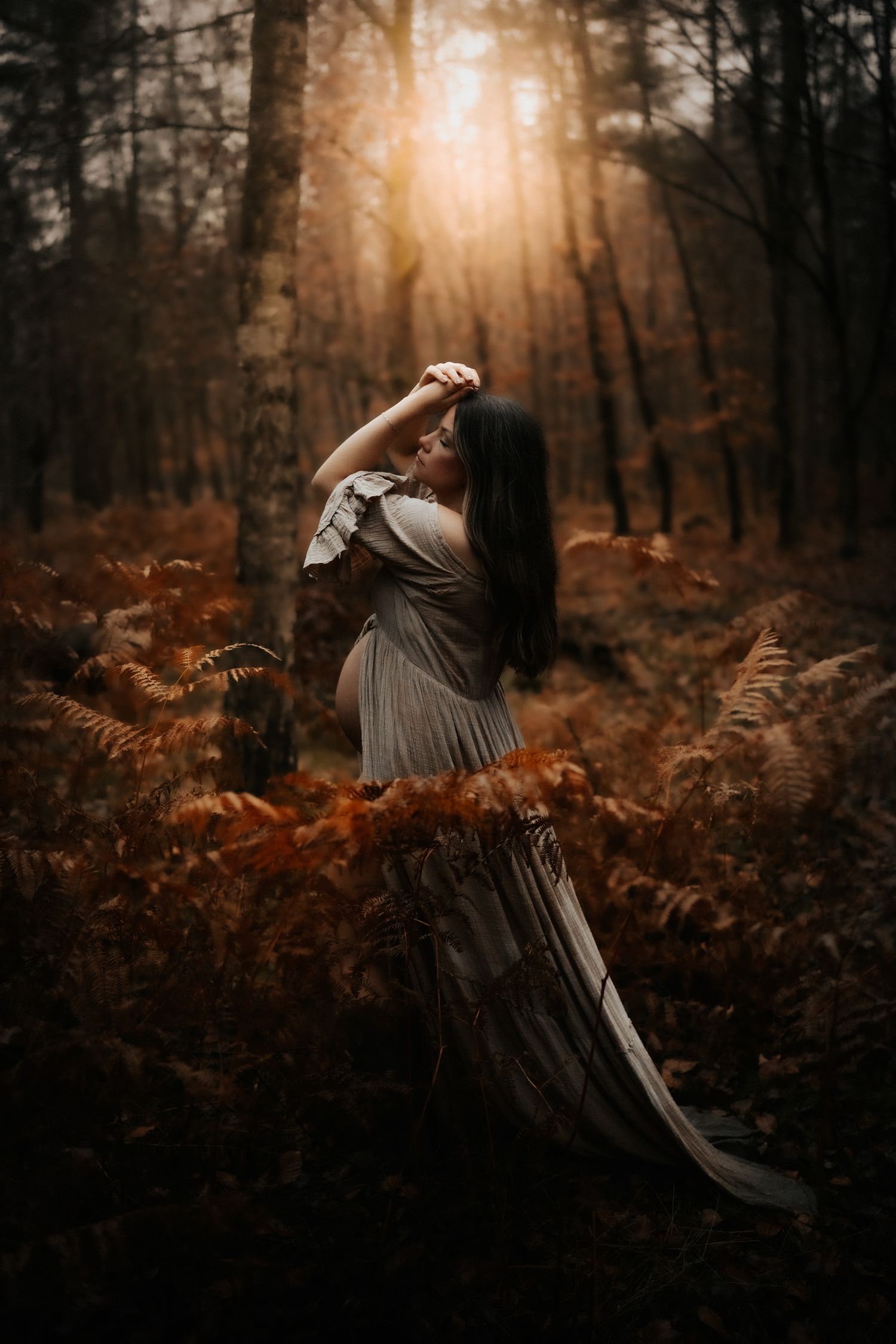 A figure in a flowing dress dances gracefully among autumn foliage in a misty forest at sunset.