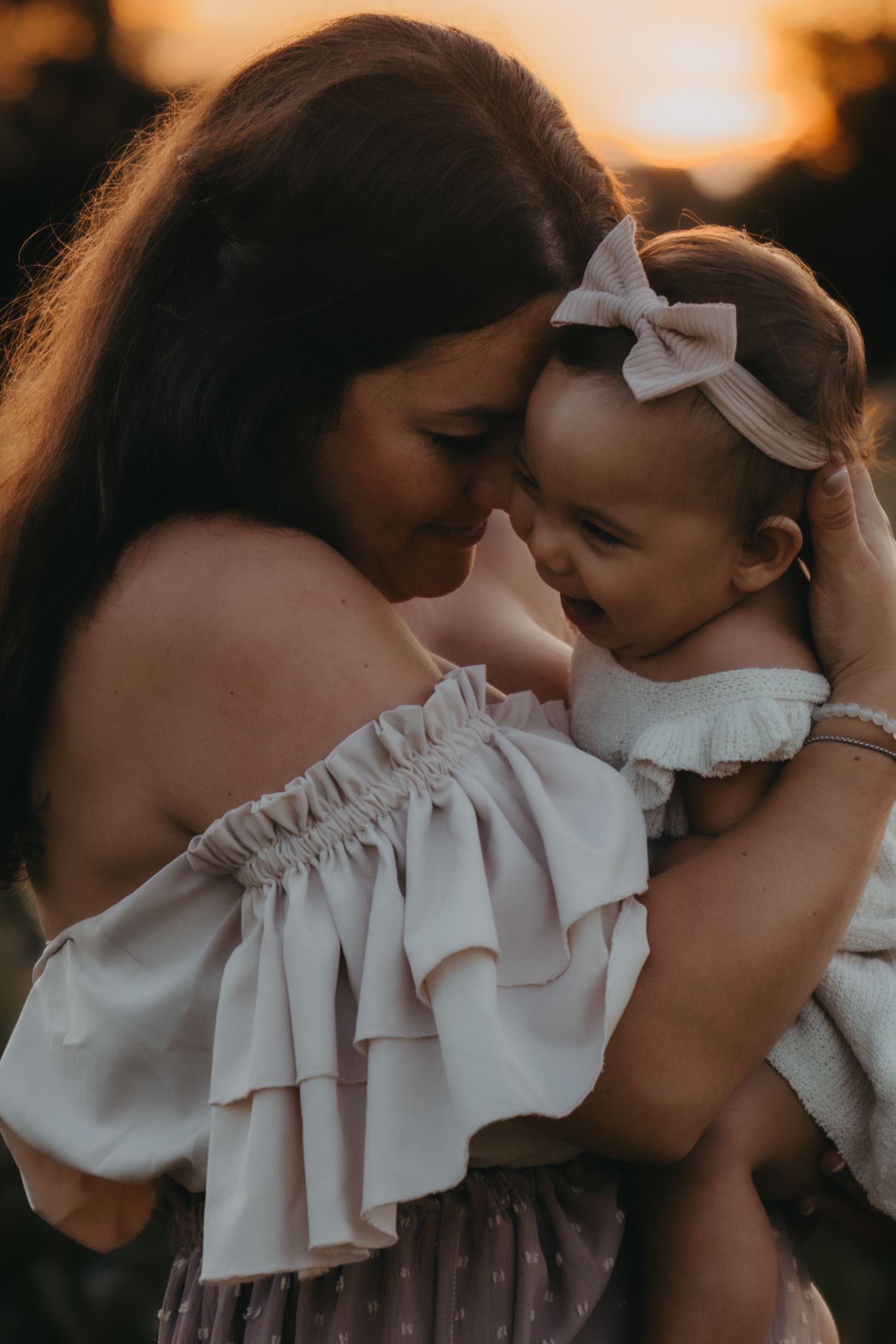 An intimate embrace between parent and baby in white dresses during golden hour.