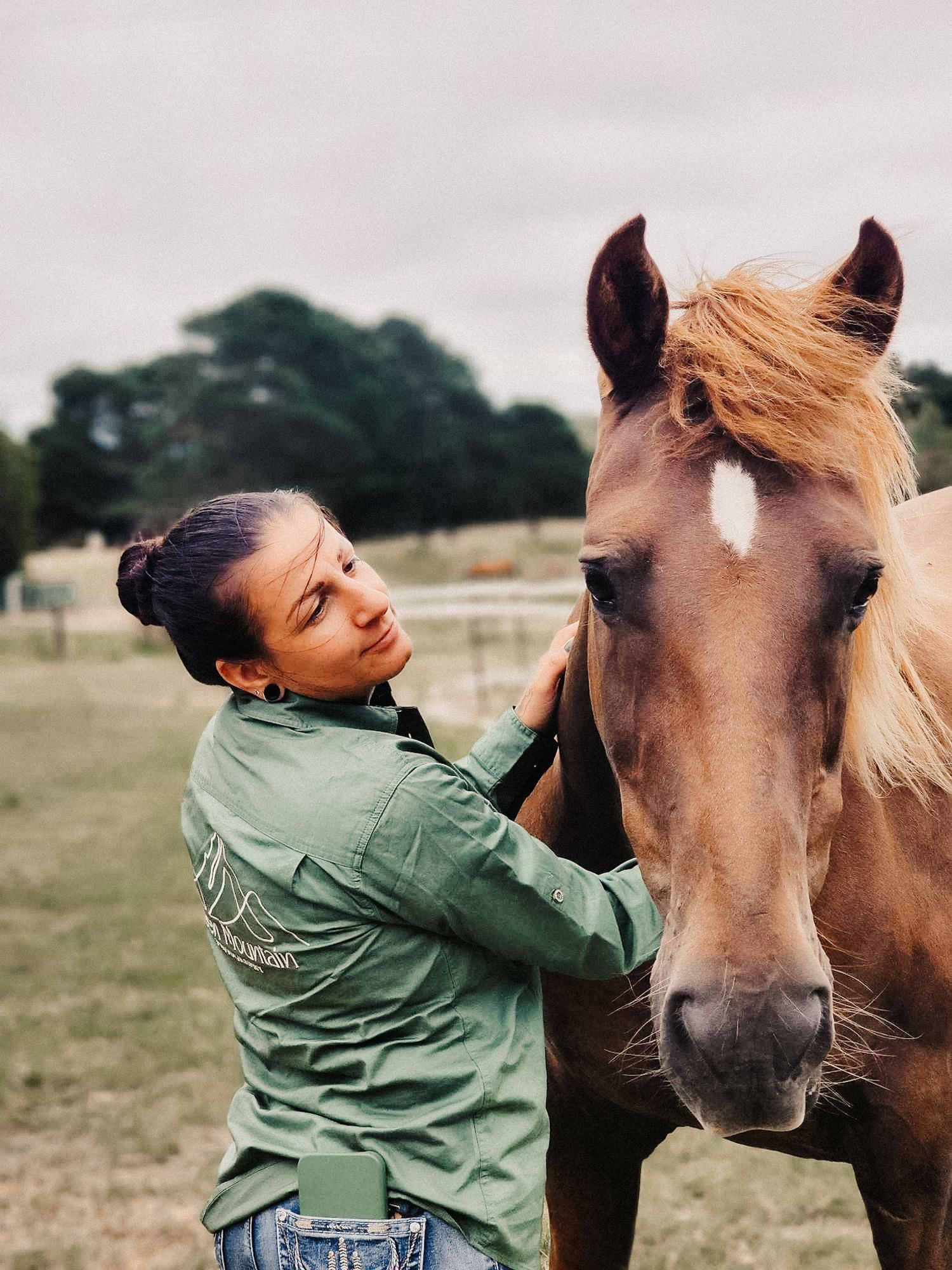 Person in green jacket bonding with a brown horse with blonde mane in a field.