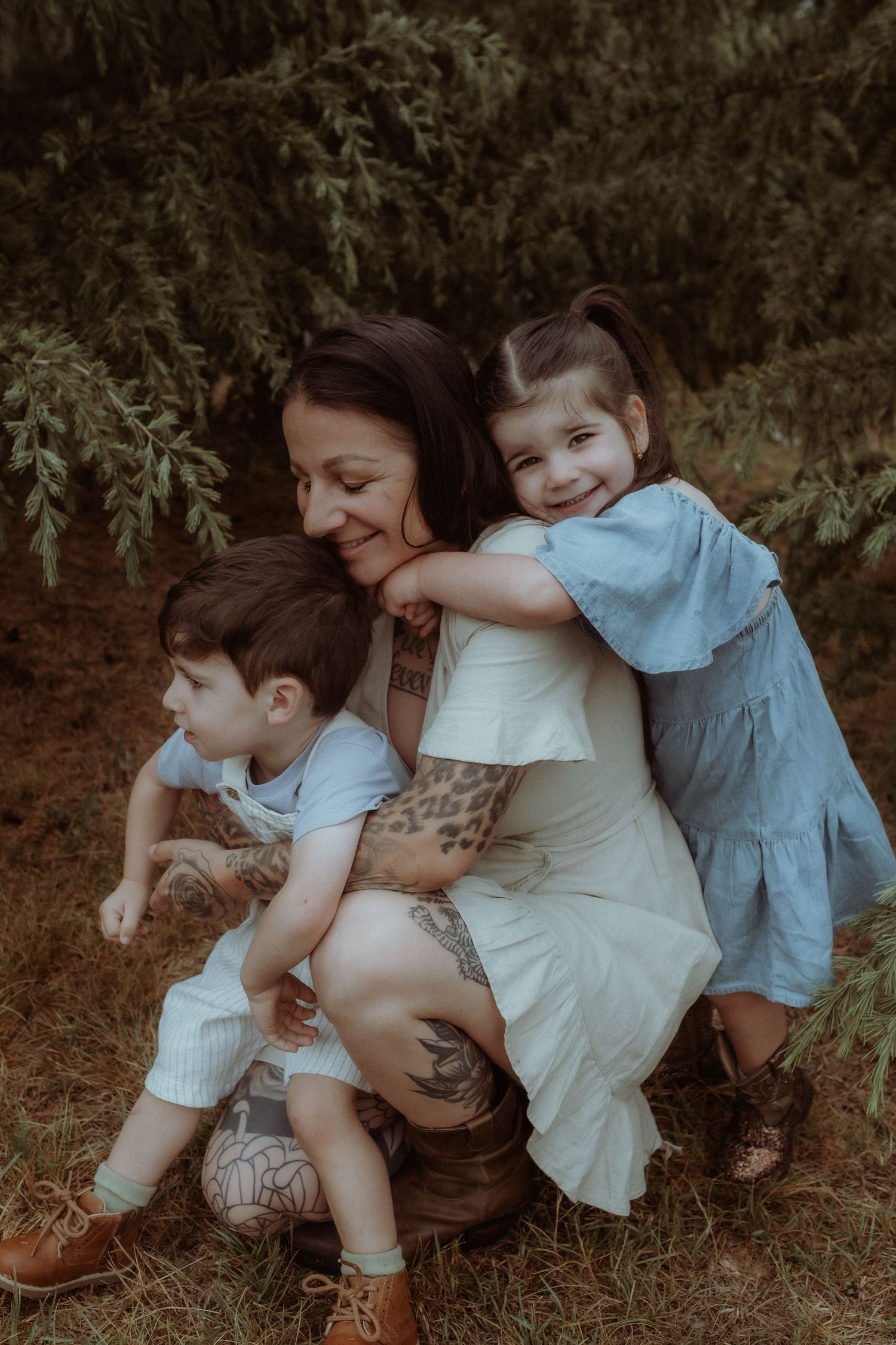 Family portrait in moody lighting against evergreen trees outdoors.
