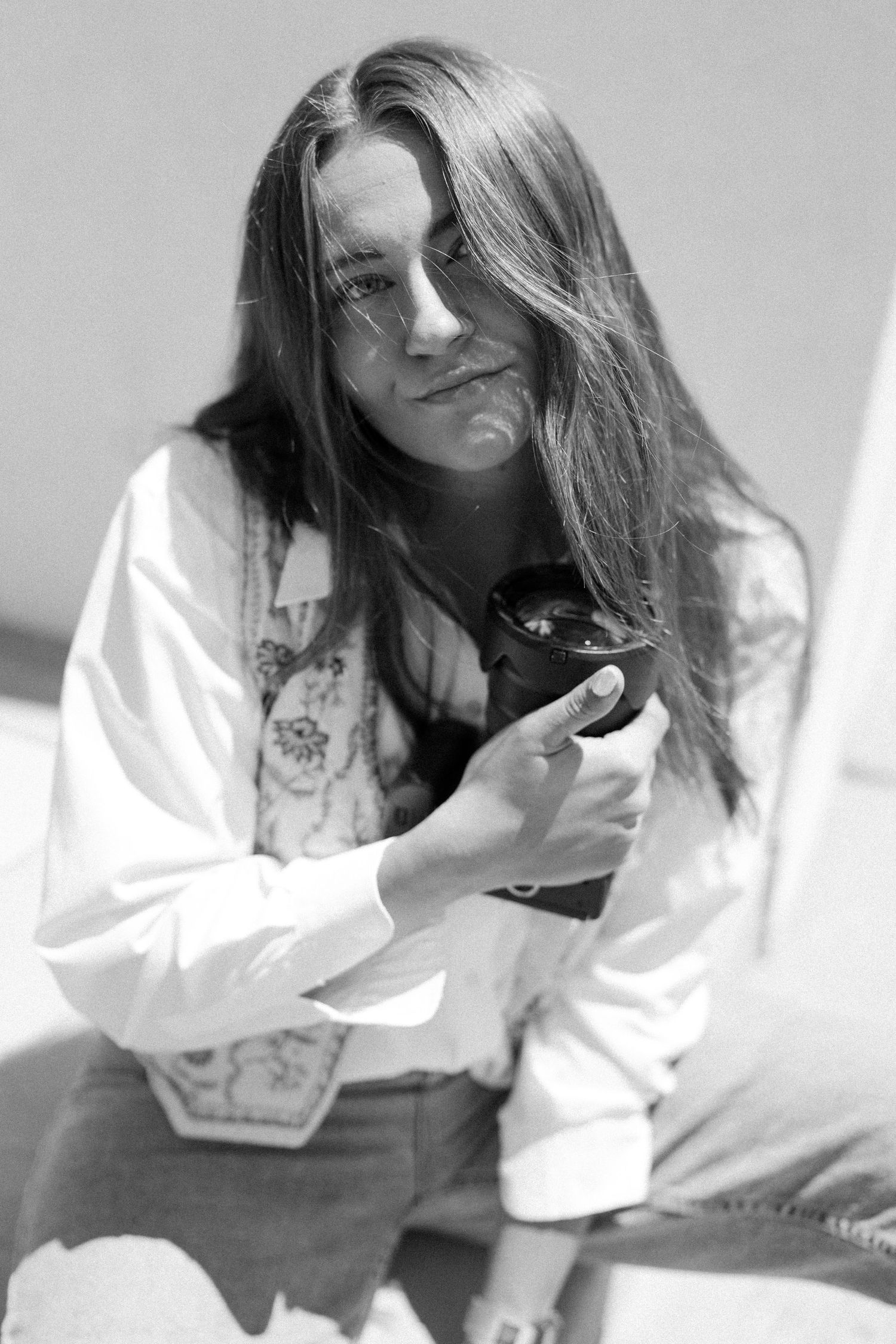 Portrait of a person in white jacket with long dark hair against neutral background in black and white.