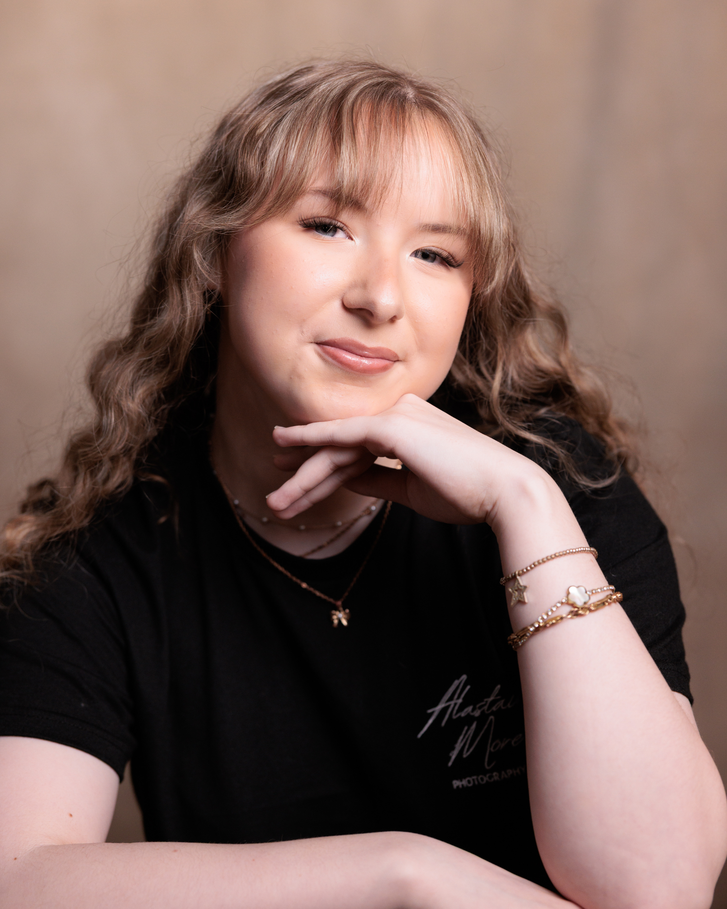 Portrait of someone in a black t-shirt with wavy blonde hair, resting their chin on their hand against a neutral background.