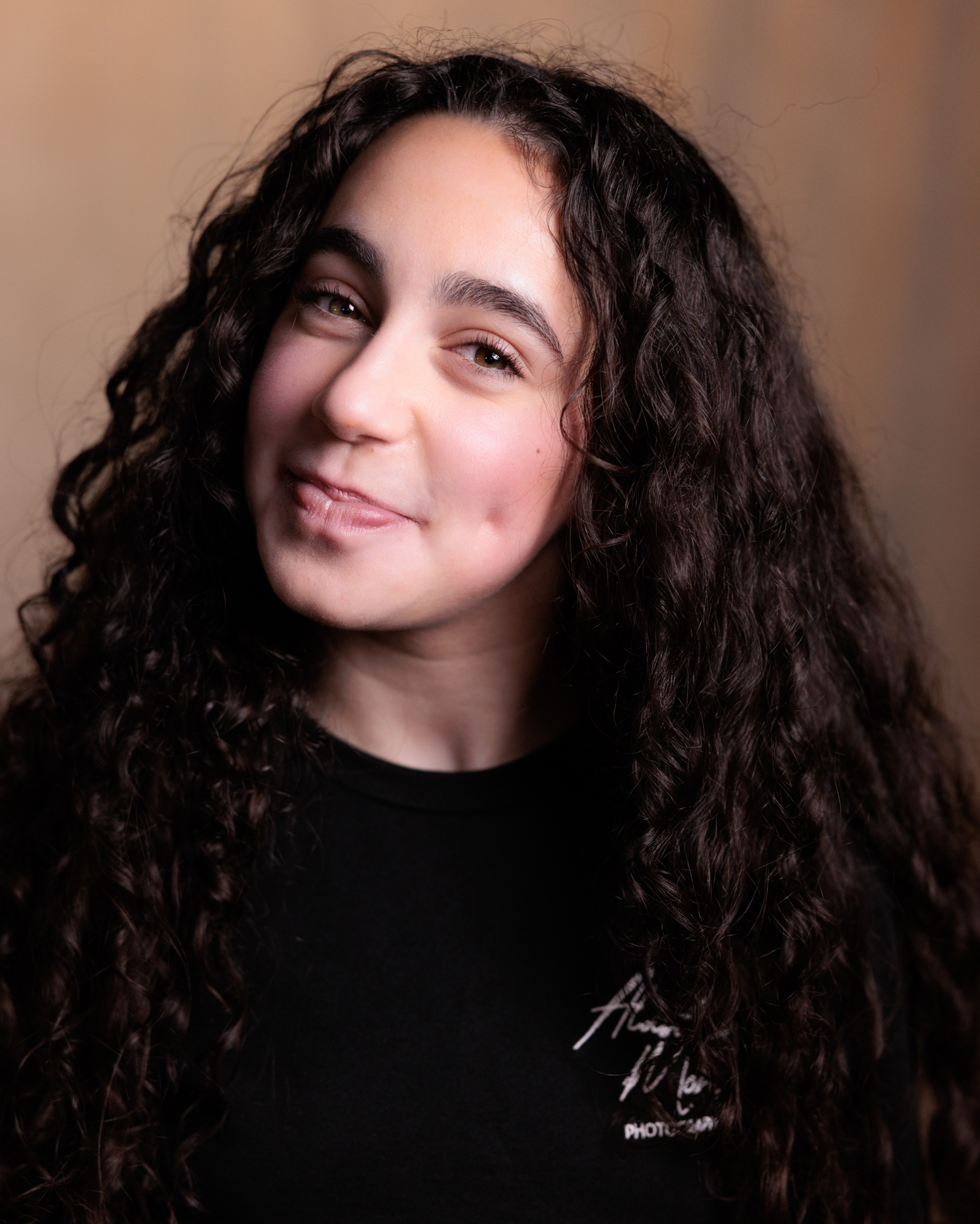 A series of portraits showing someone with long dark curly hair against a dark background making playful expressions.