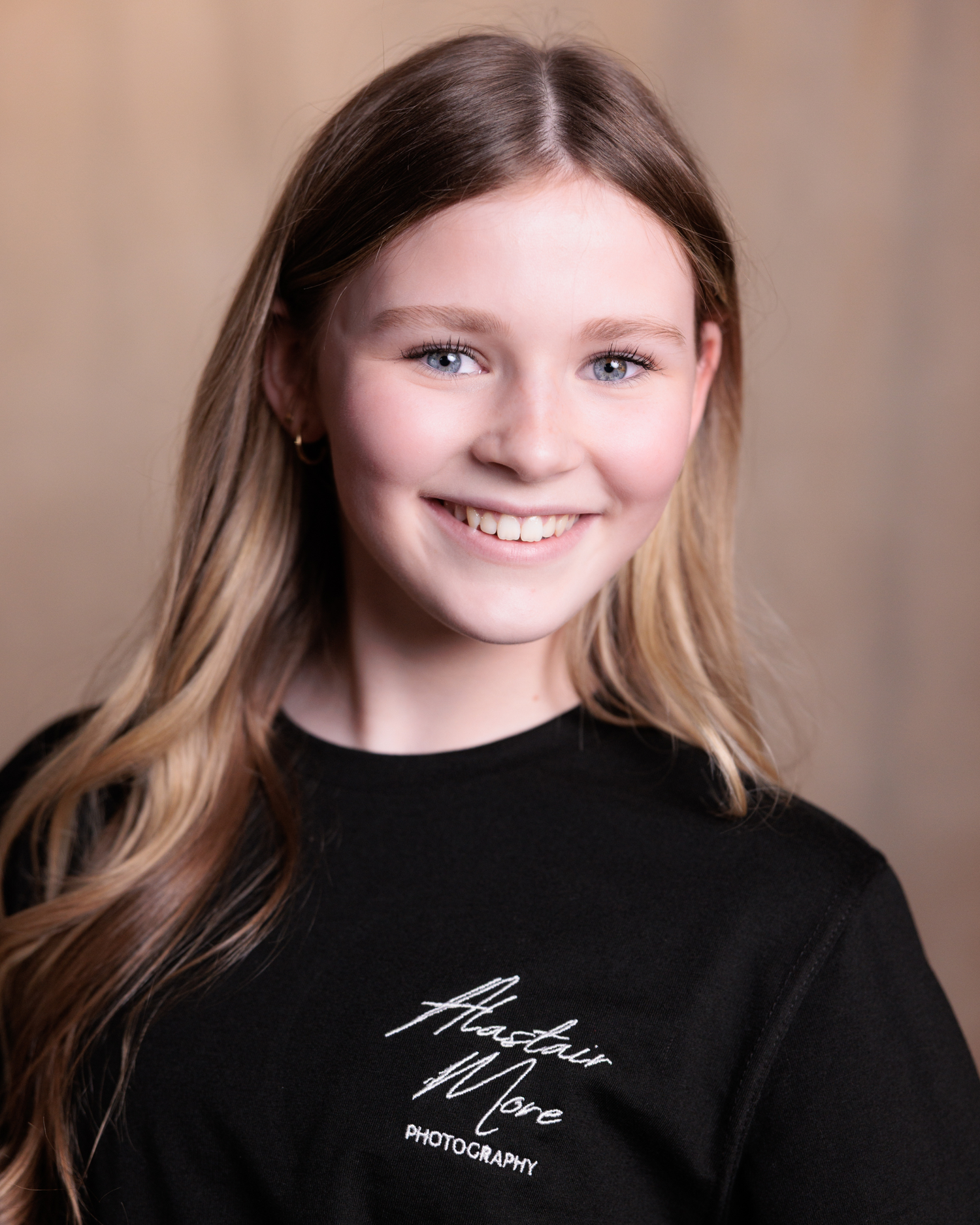Studio portrait of a person with long blonde hair wearing a black shirt with text against a neutral brown background.