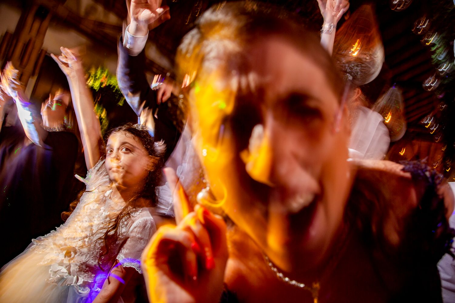 Guests dancing joyfully at a lively wedding reception party with colorful lights and festive atmosphere.