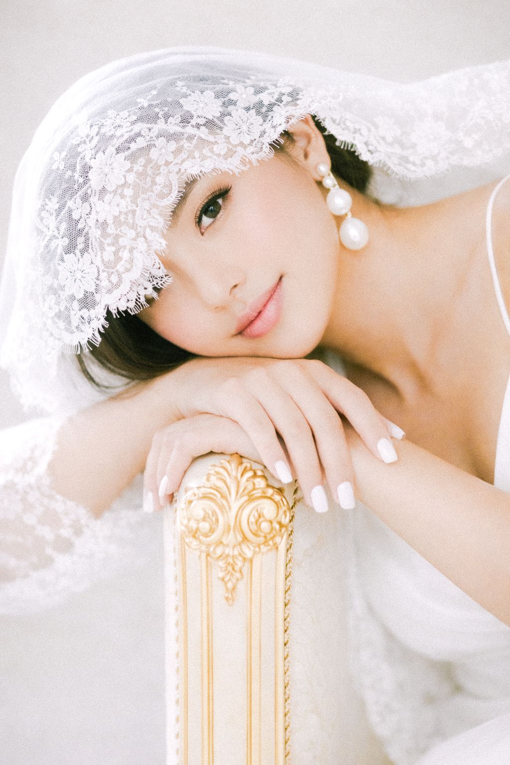 Elegant bridal portrait with delicate lace veil and pearl earrings resting on ornate gold furniture.