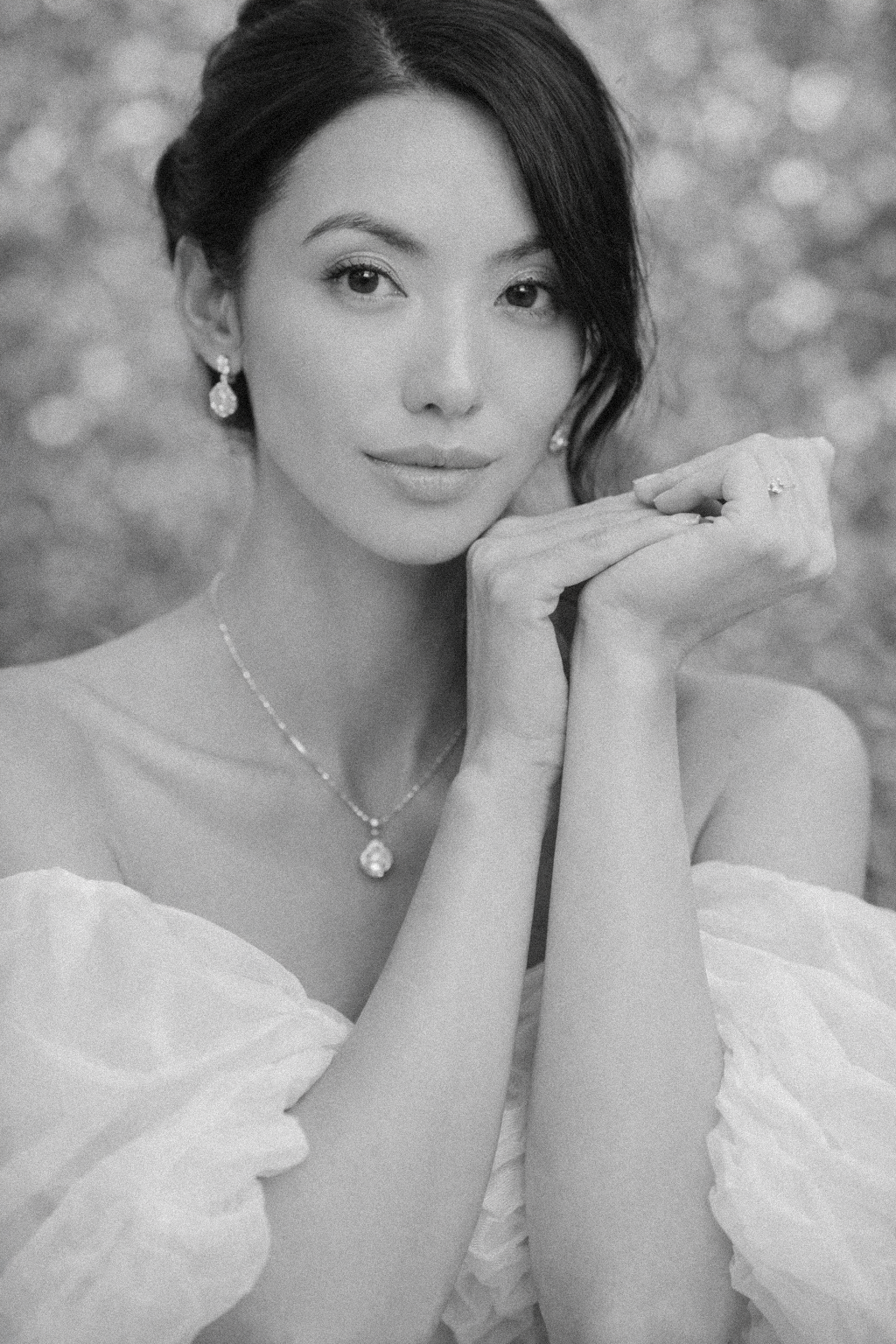 Black and white portrait of a woman in a white dress wearing delicate pearl jewelry against a soft bokeh background.