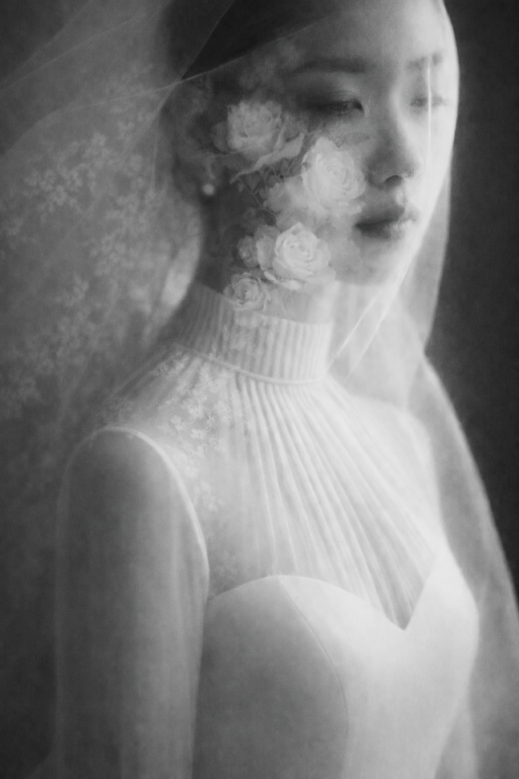 Black and white bridal portrait of a woman in a white gown and lace veil with floral details.