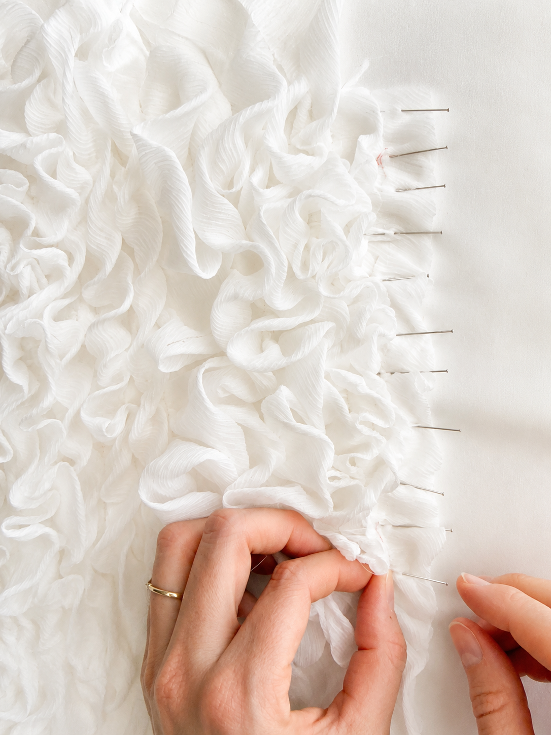 Hands pinning white ruffled fabric with straight pins during bridal gown or dress construction.