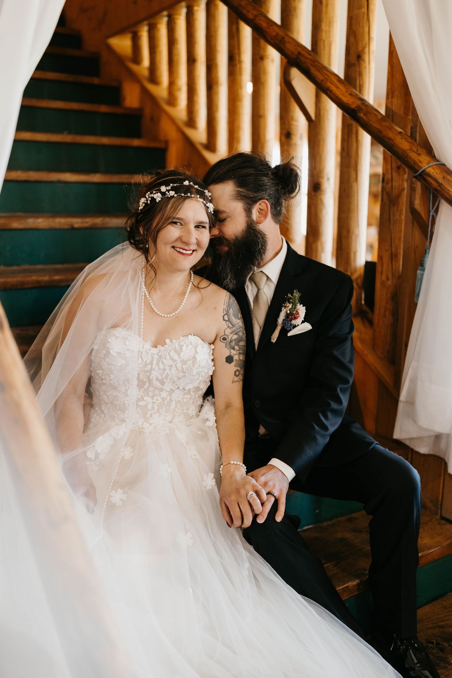 Bride and groom sitting on rustic wooden staircase, sharing a tender moment in a log cabin wedding venue.