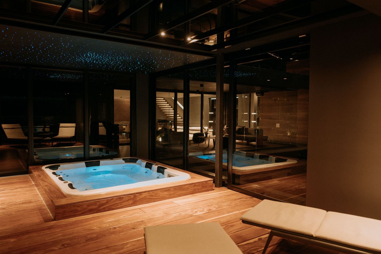 Elegant indoor jacuzzi on wooden deck with glass walls and ambient star ceiling lighting at night.