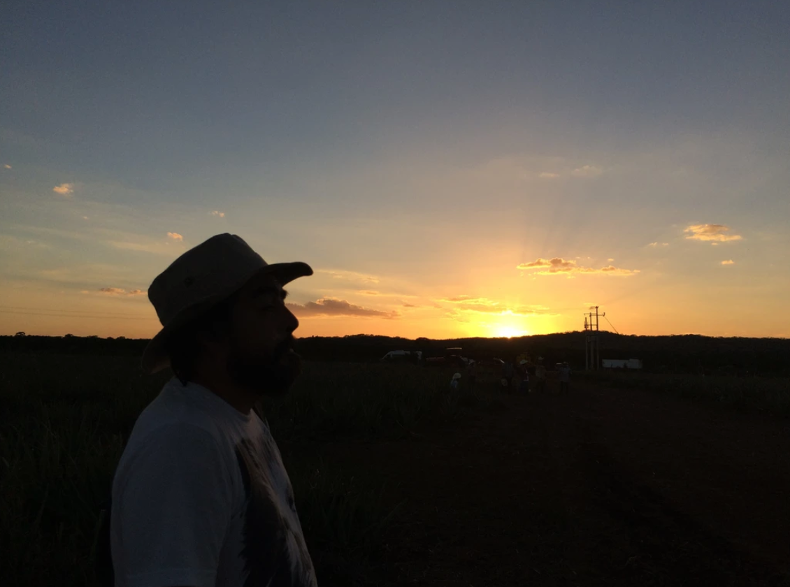 Silhouette of a man in a cowboy hat watching a vibrant sunset over open fields.