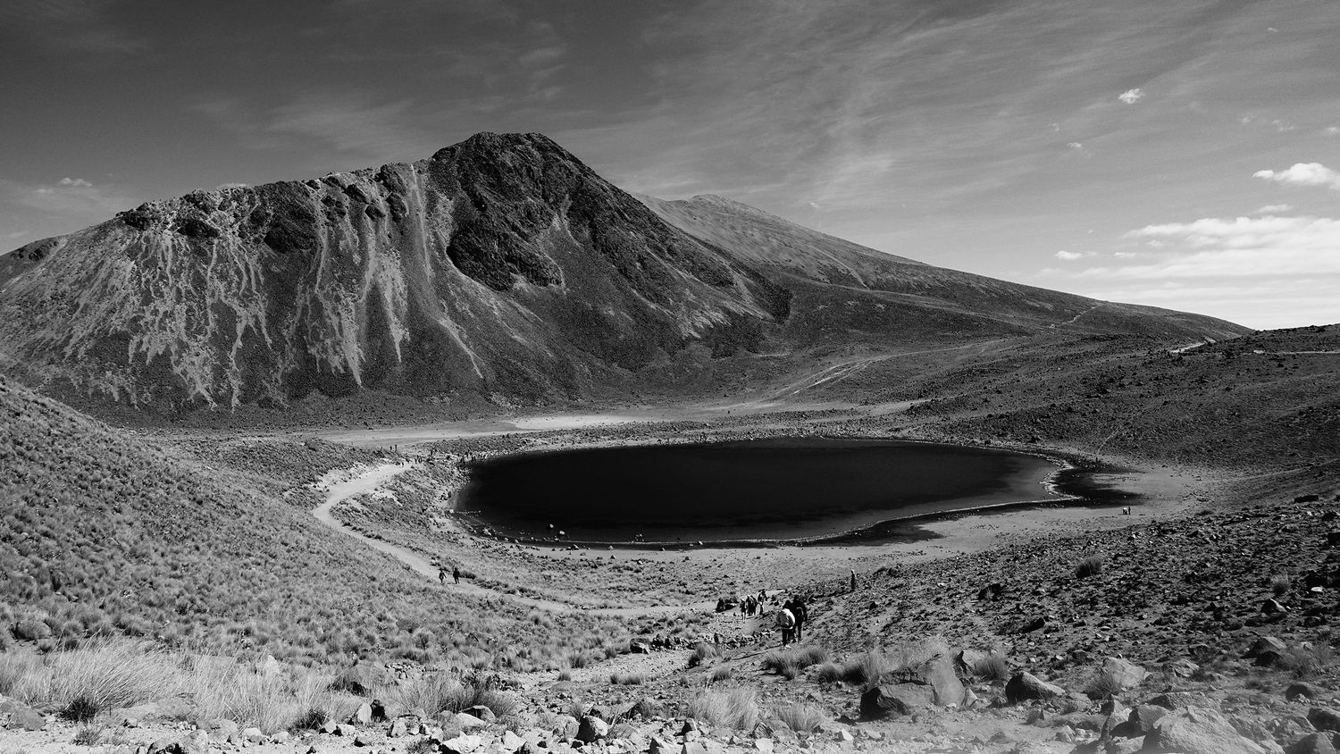 Black and white aerial view of volcanic crater lake on rugged mountain.