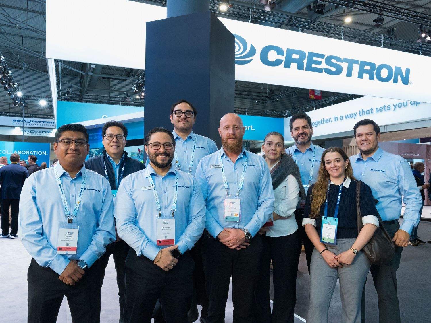 Team of nine professionals posing together at the Crestron trade show exhibit booth.