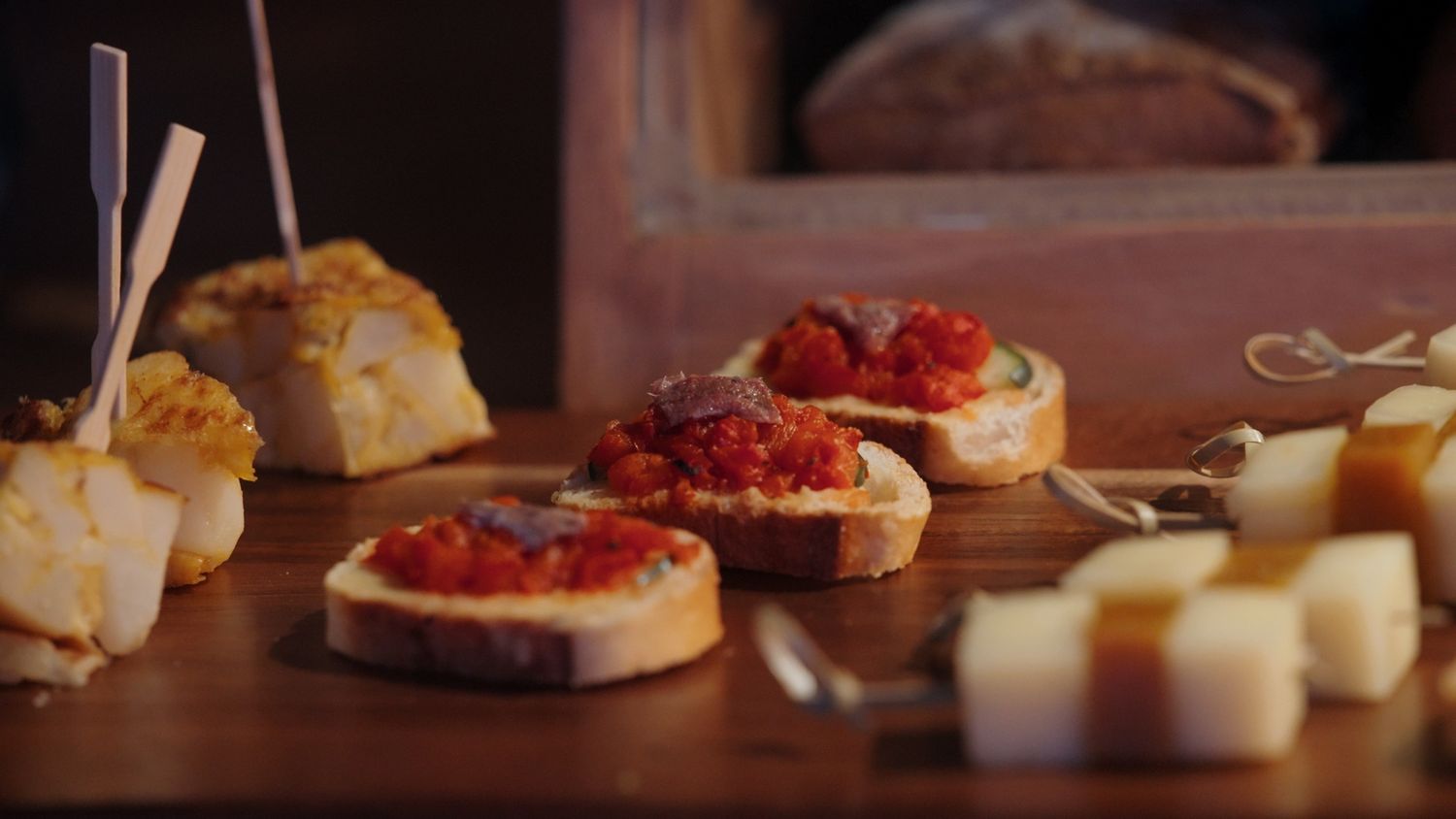 Bruschetta topped with tomato and cheese appetizers on a wooden board with cubed cheese.