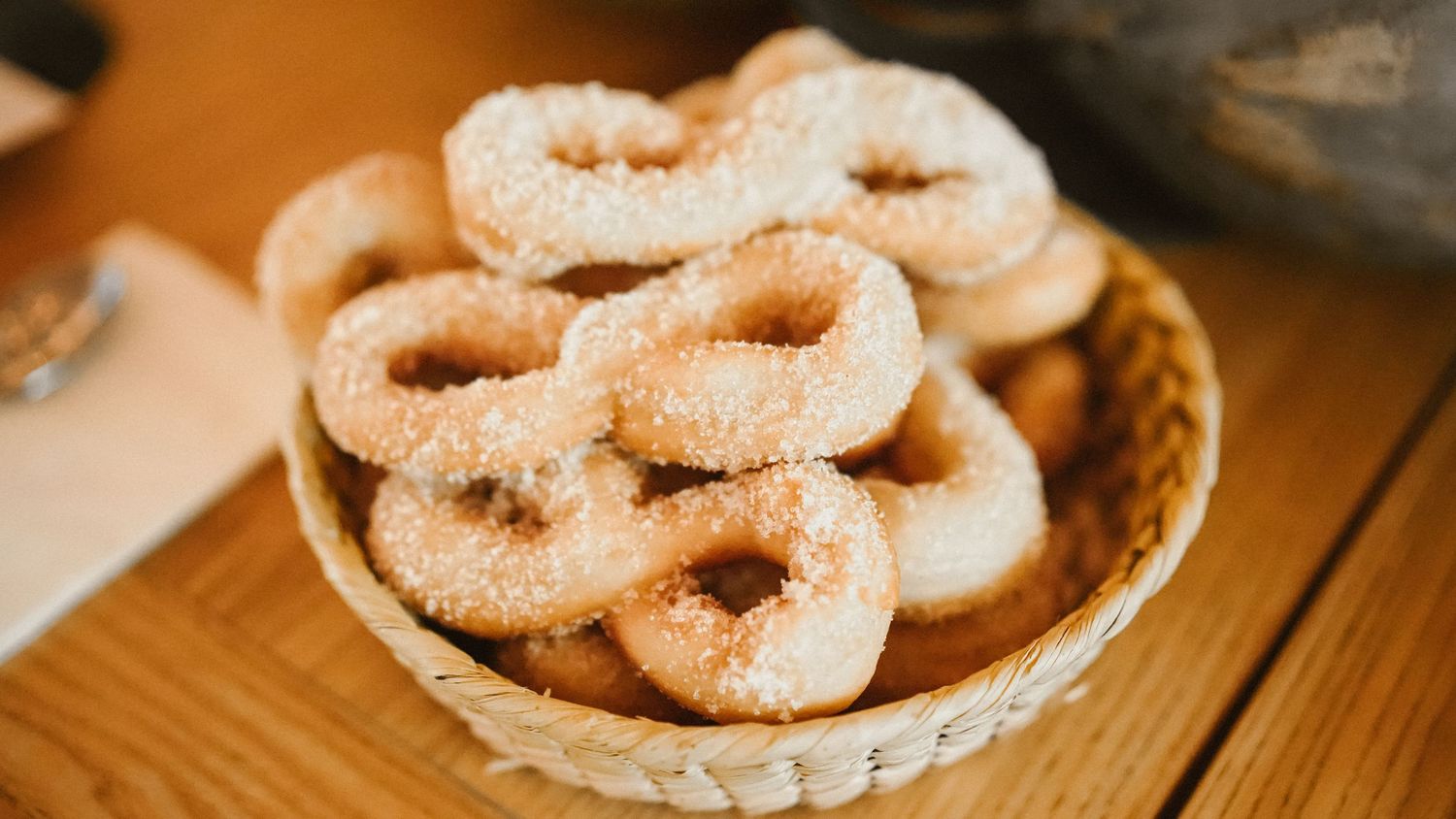 Wicker basket filled with sugar-coated ring-shaped donuts on a wooden surface.