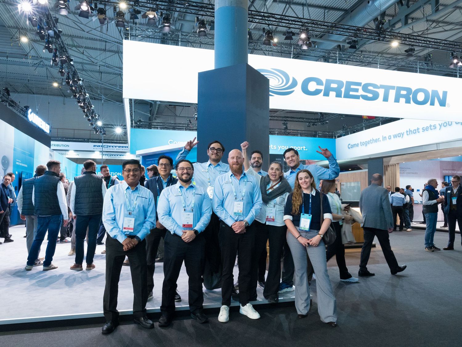 Team of ten employees celebrating at the Crestron exhibition booth at a trade show.