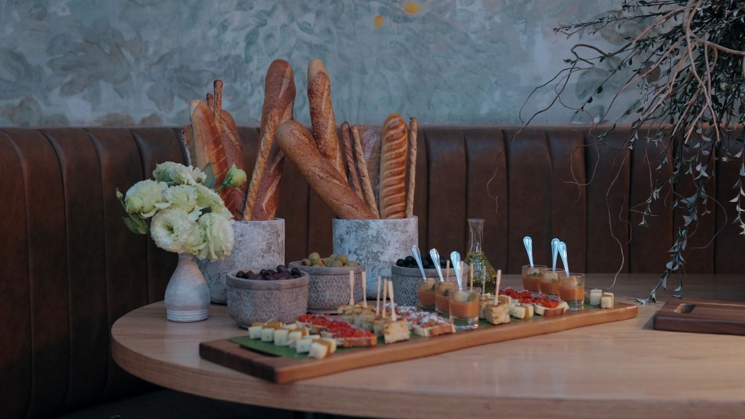 Elegant charcuterie board with baguettes, jams, and fresh toppings on a wooden table in a cozy restaurant.