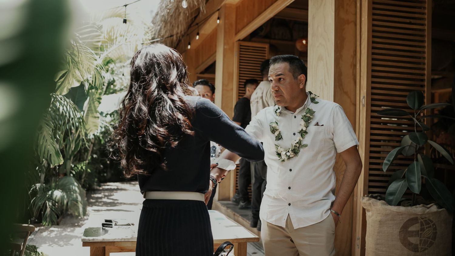 Man wearing floral lei greeting woman at a tropical themed indoor venue.