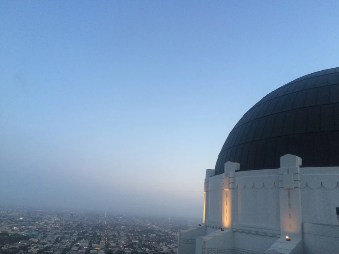 Griffith Observatory dome illuminated at dusk with the Los Angeles cityscape in the background.