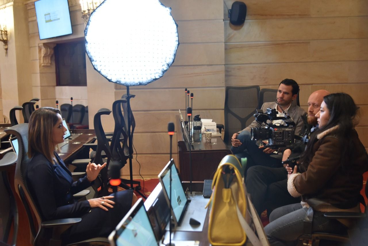 Film crew with camera and lighting equipment interviewing woman at ornate indoor location.