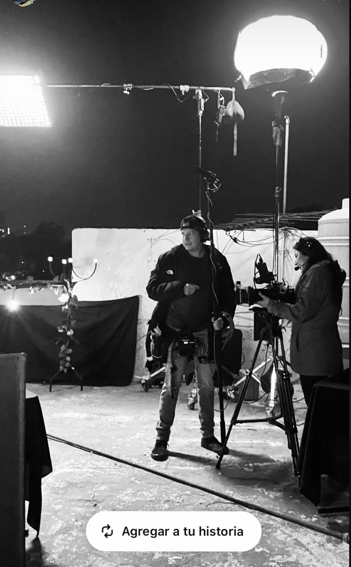 Black and white nighttime film set with crew operating professional camera under large balloon lighting equipment.