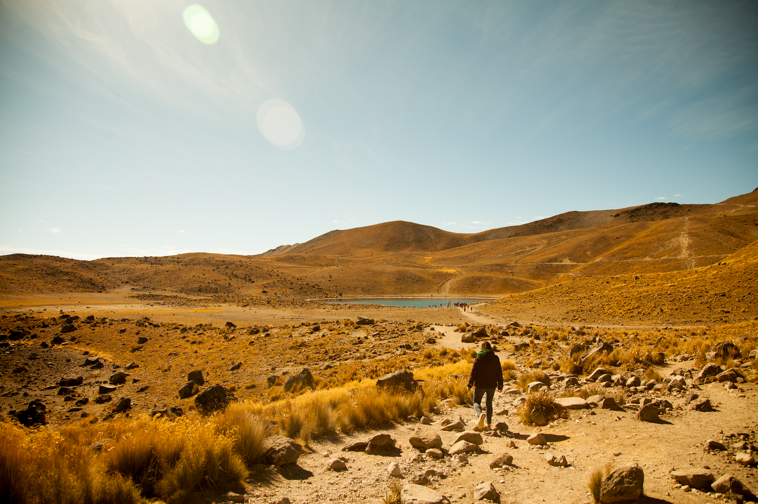 Hiker walking through arid Andean landscape toward a turquoise lake.