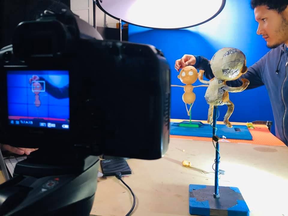 A filmmaker photographs a handmade puppet figure against a blue screen in a professional studio setup.