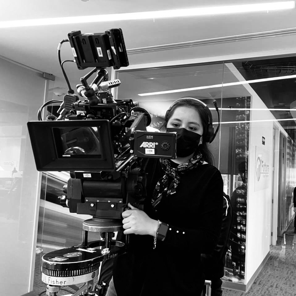Black and white photo of female cinematographer operating professional ARRI camera on film set.