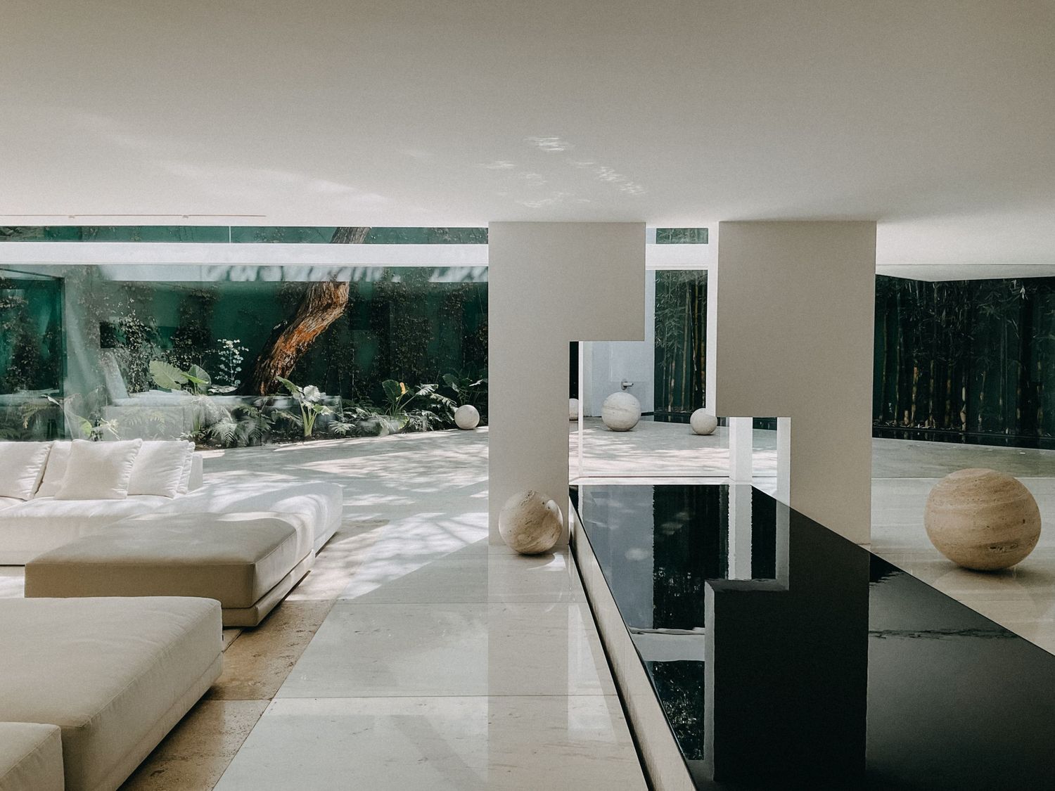 Contemporary open-plan living room with black reflective floor, white sofa, and garden views.