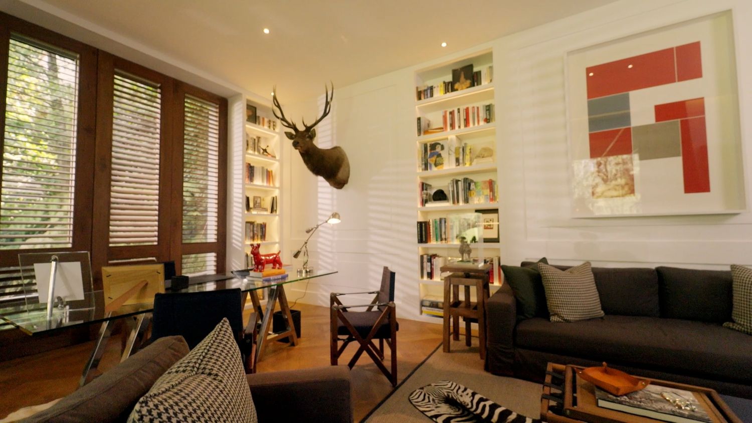 Stylish living room with deer head mount, bookshelves, dark sofas and eclectic decor.