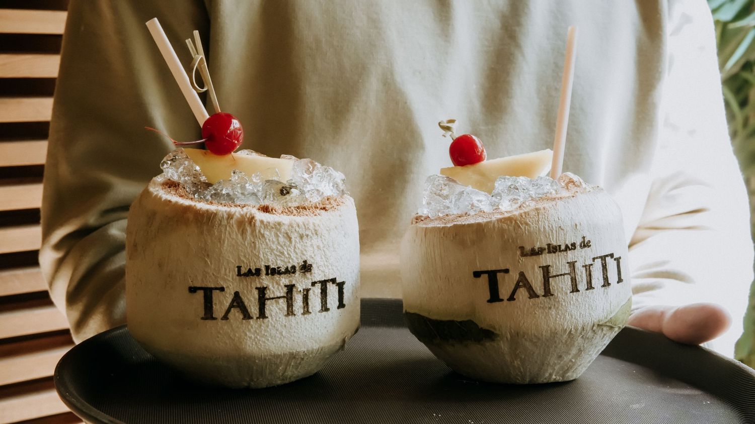 Two coconut cups branded Las Islas de Tahiti filled with tropical cocktails garnished with cherries and straws.