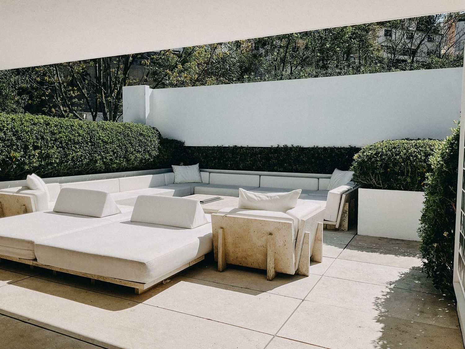 Elegant outdoor patio with white sectional sofa, lounge beds, and manicured hedge walls.