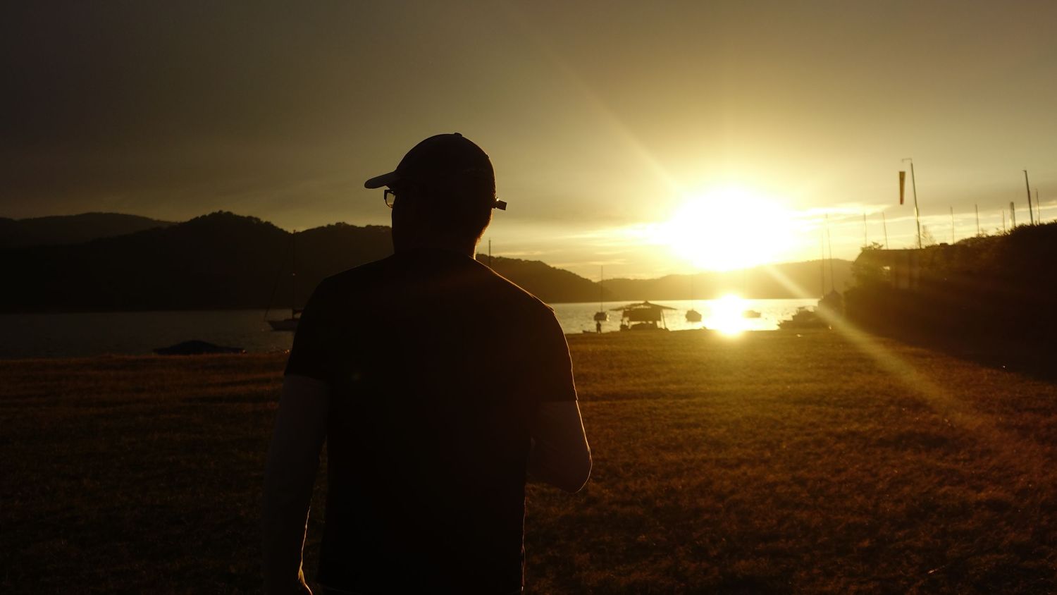A silhouetted man watches a breathtaking golden sunset over a scenic lakeside landscape.