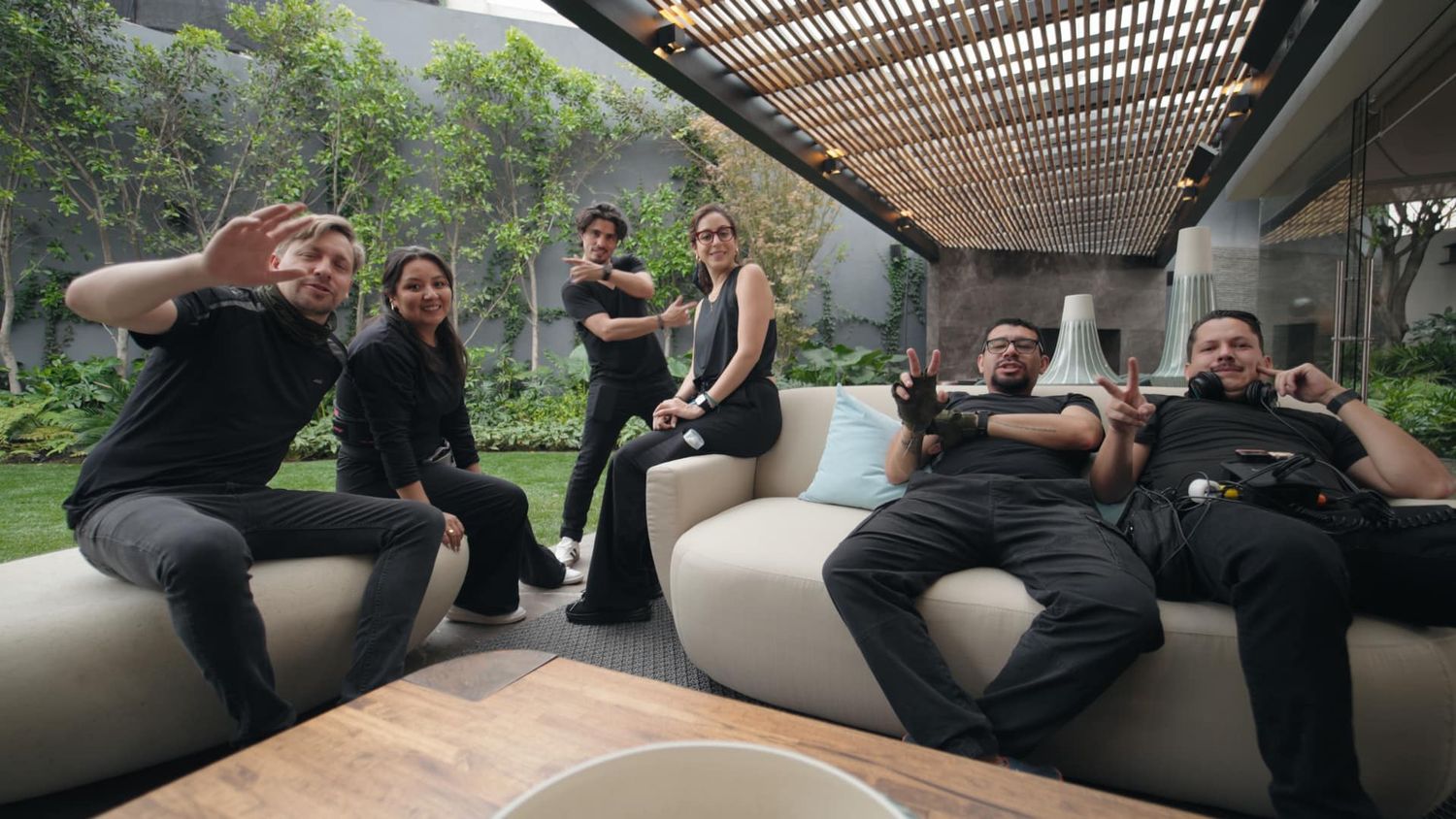 Group of six film production crew members relaxing on outdoor patio furniture in a modern garden setting.