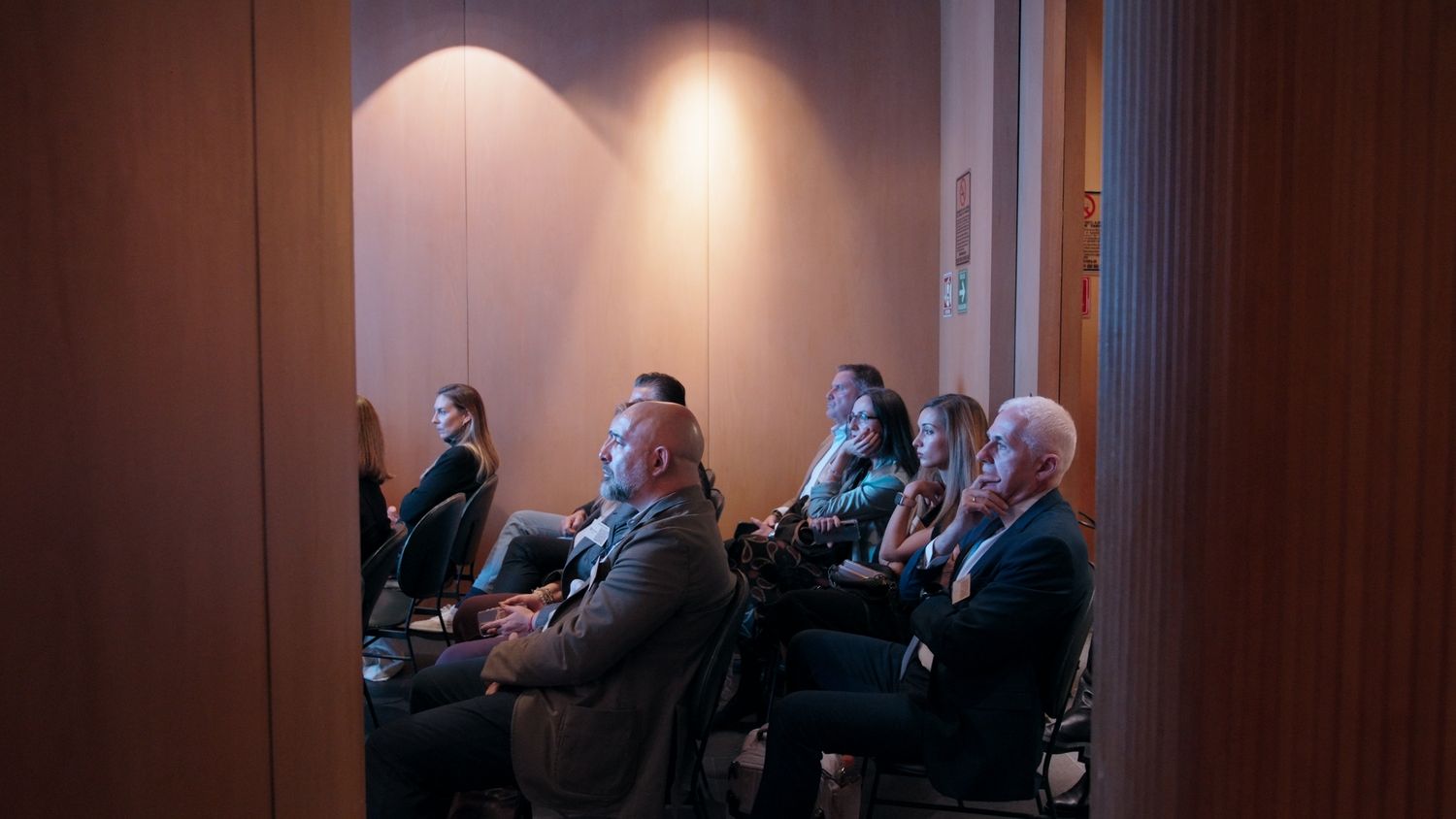 Audience members seated in a dimly lit conference room, attentively watching a presentation during a business event.