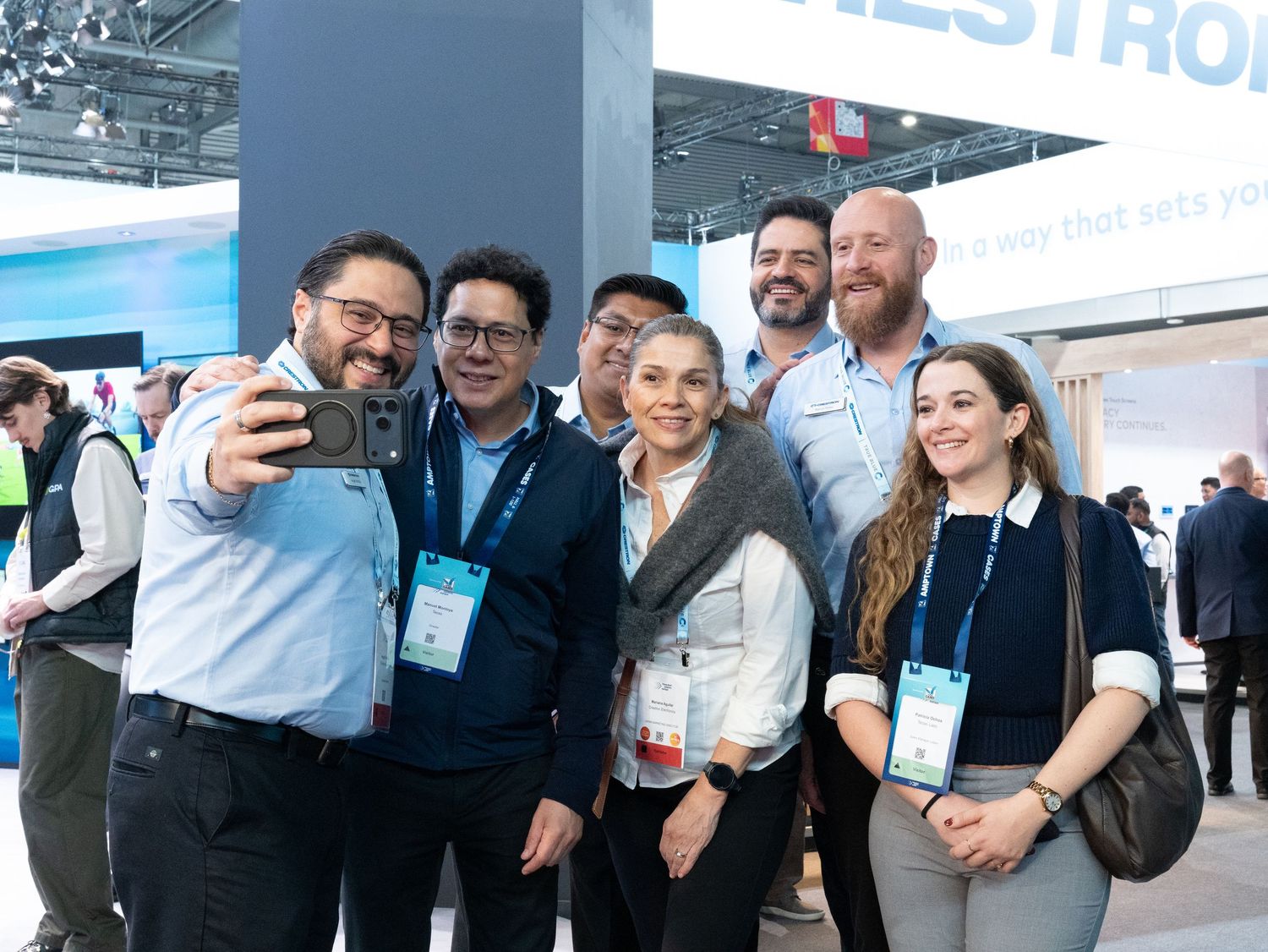 Group of seven smiling colleagues taking a selfie at the Crestron trade show booth.