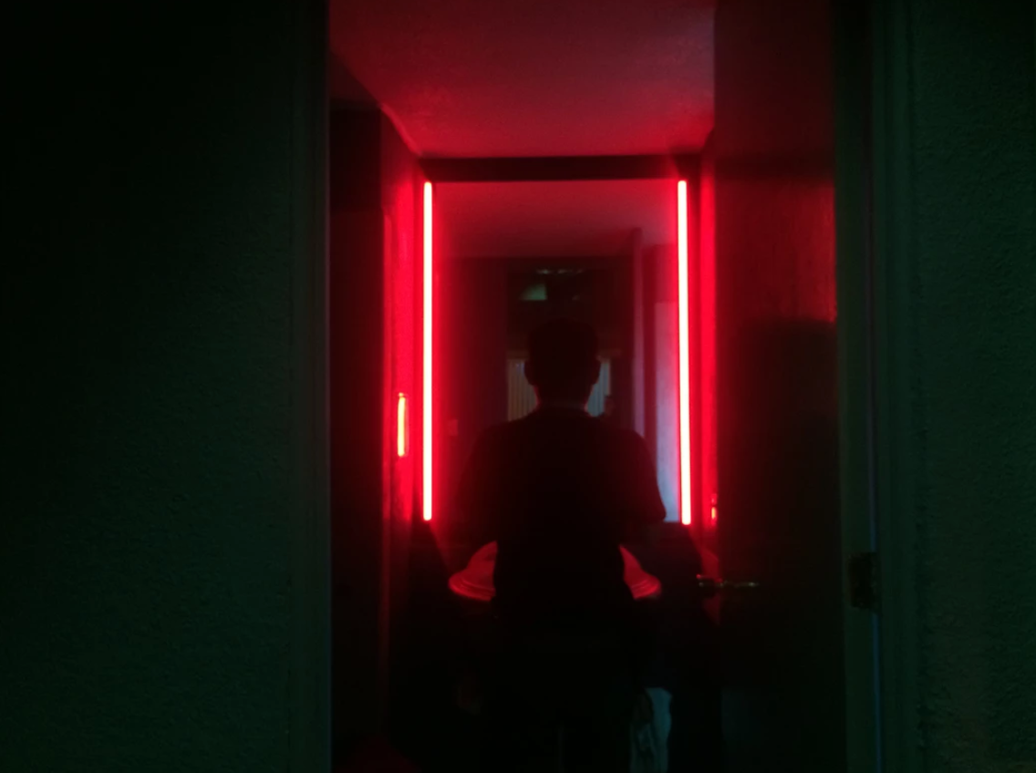Silhouette of person standing in dark hallway illuminated by red neon lights.