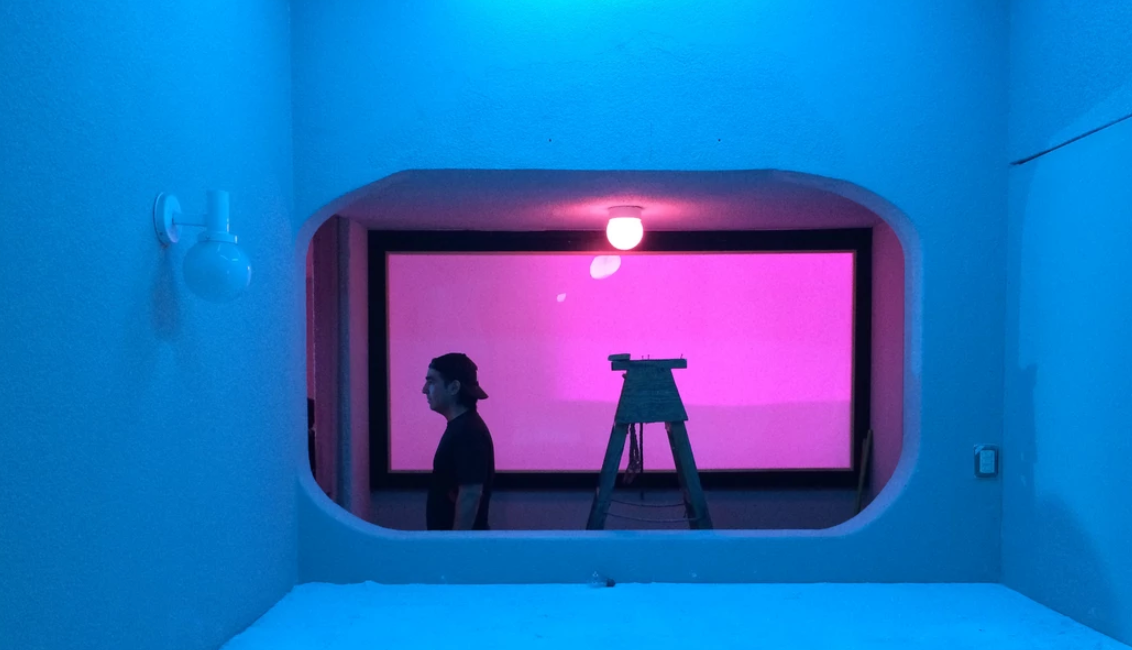 Person standing before a glowing pink window display in a blue-lit modern art installation.