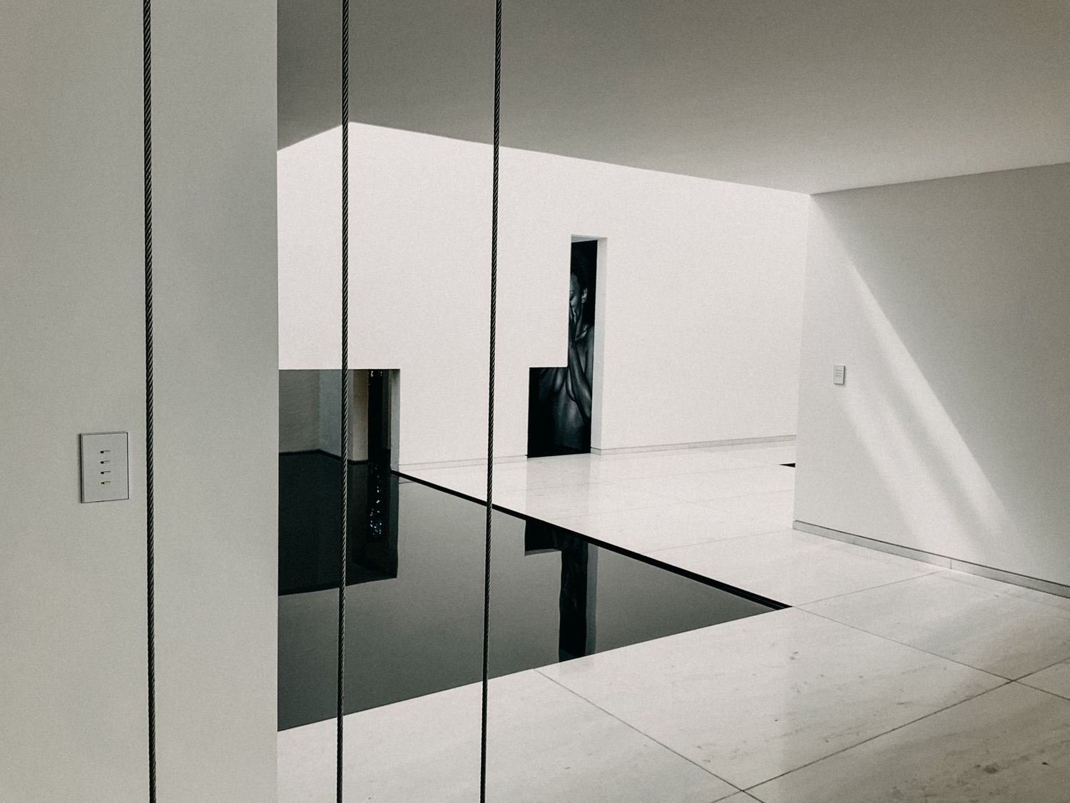 Minimalist white interior space with black reflective floor panels and geometric architectural design.