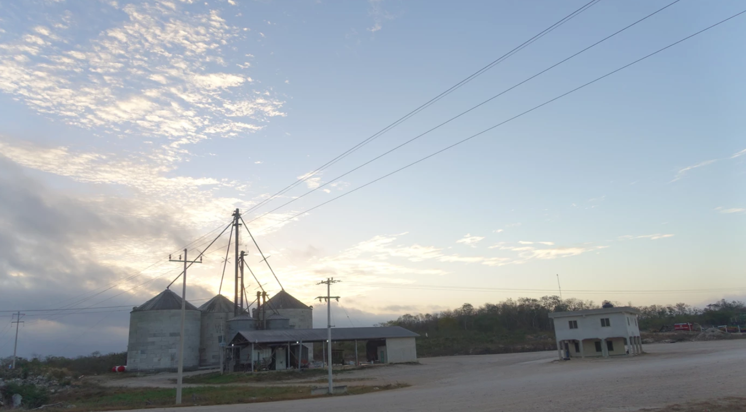 Rural farm at dusk with grain silos, utility poles, and a small building under a dramatic cloudy sky.