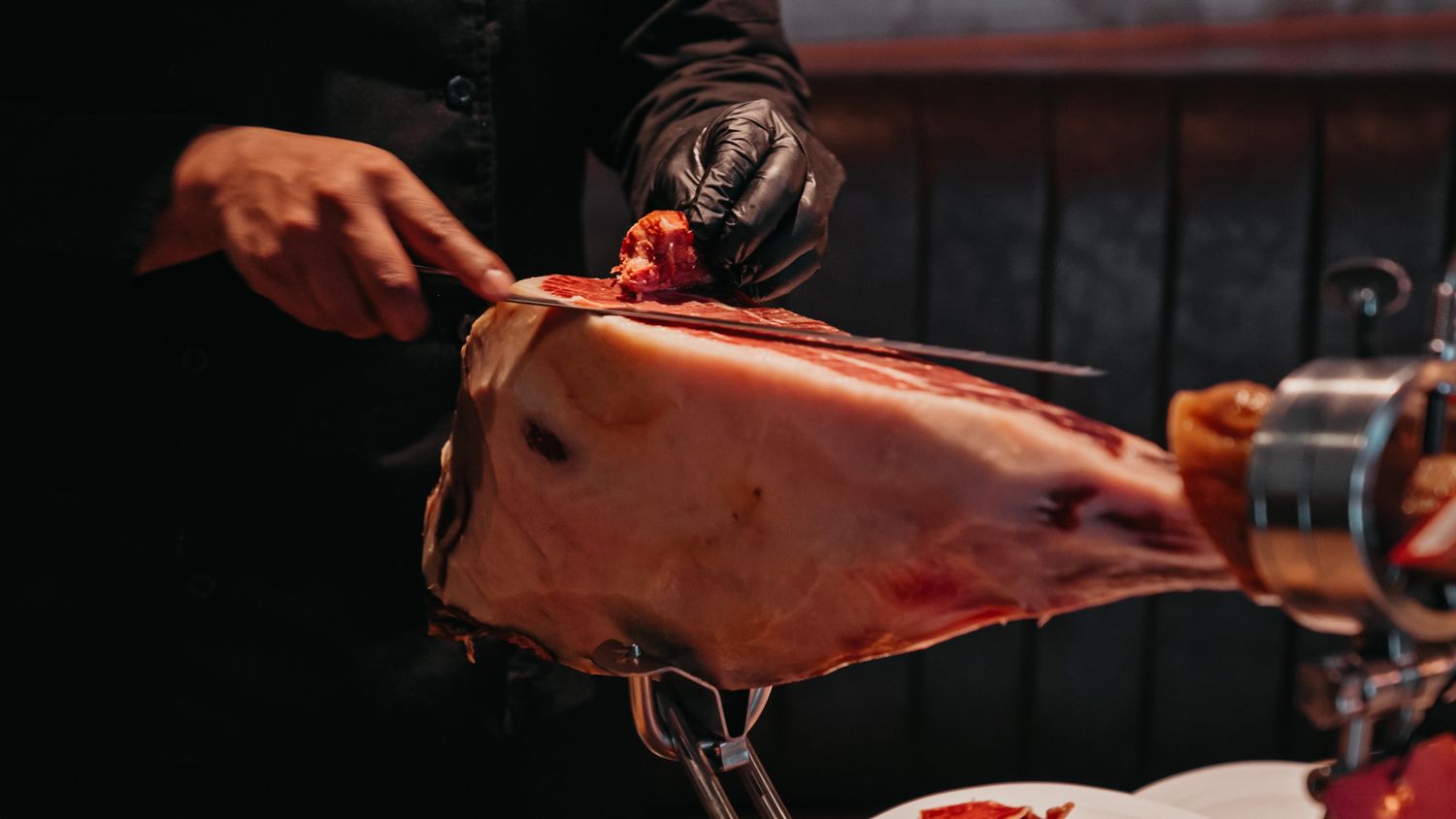 Chef slicing a whole cured Iberian ham leg at a catering event.
