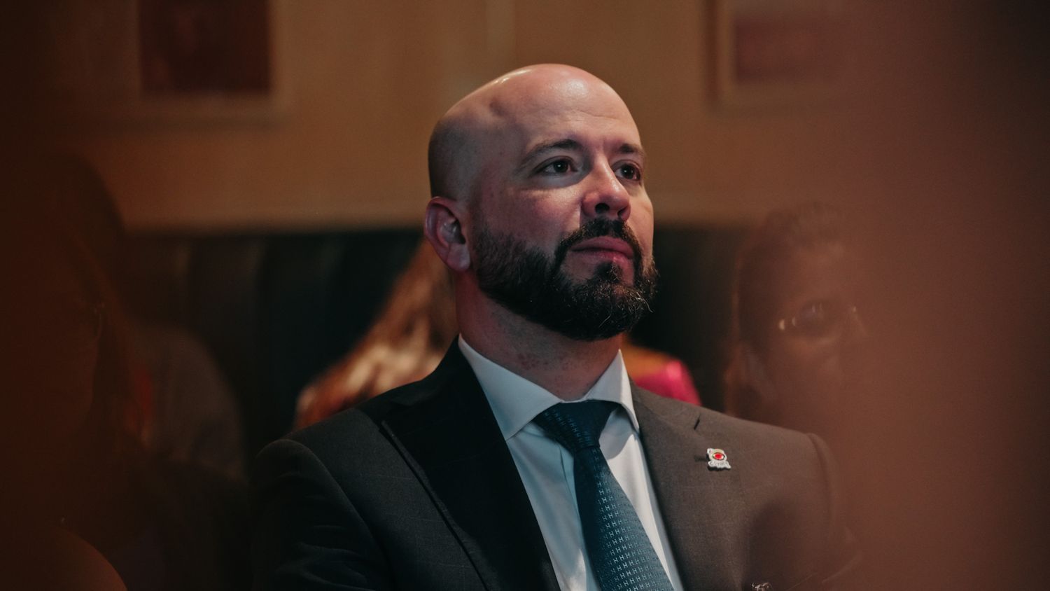 Professional man in a suit with a flag pin listening attentively at a formal event.