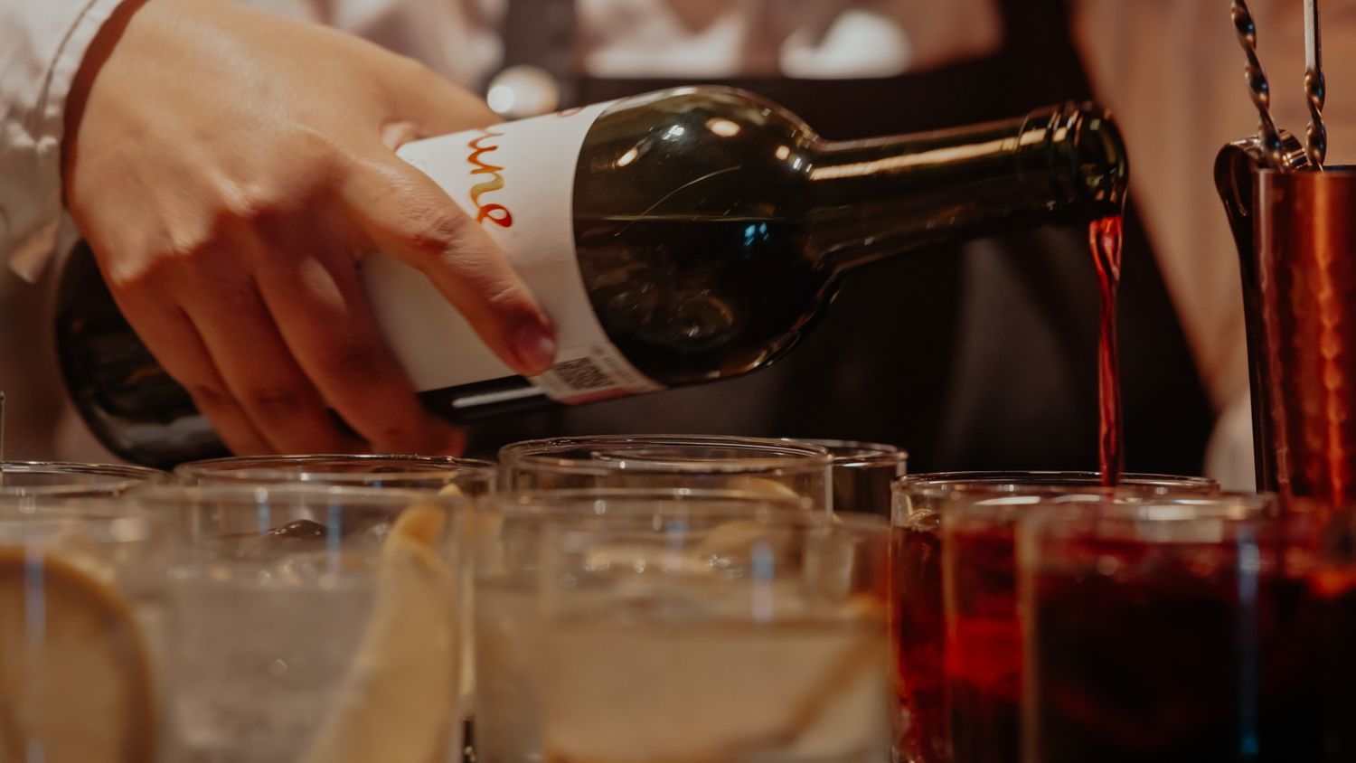 Bartender pouring red wine from a bottle into glasses at a bar event.