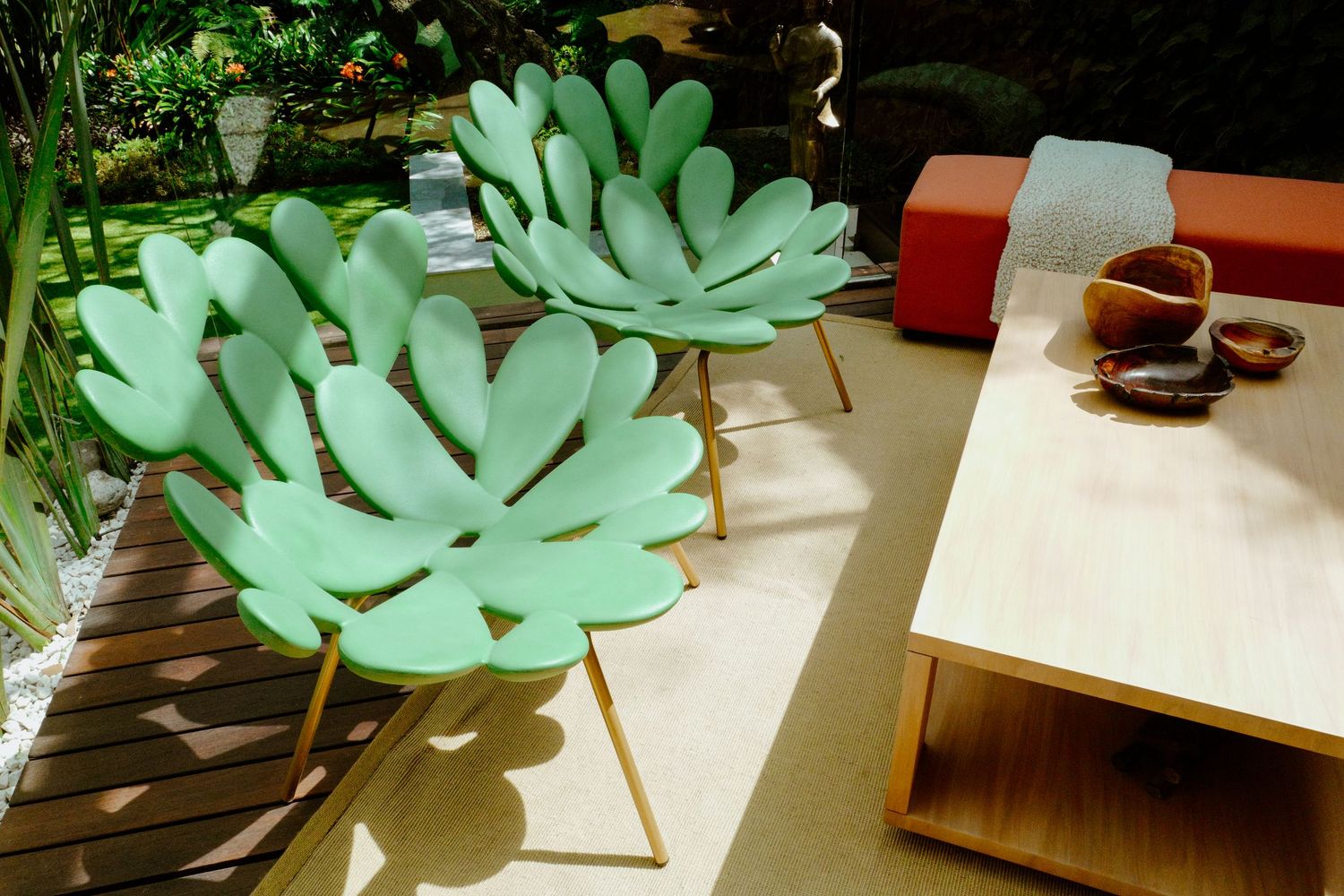 Outdoor patio with artistic monstera leaf-shaped chairs in mint green beside a wooden coffee table.
